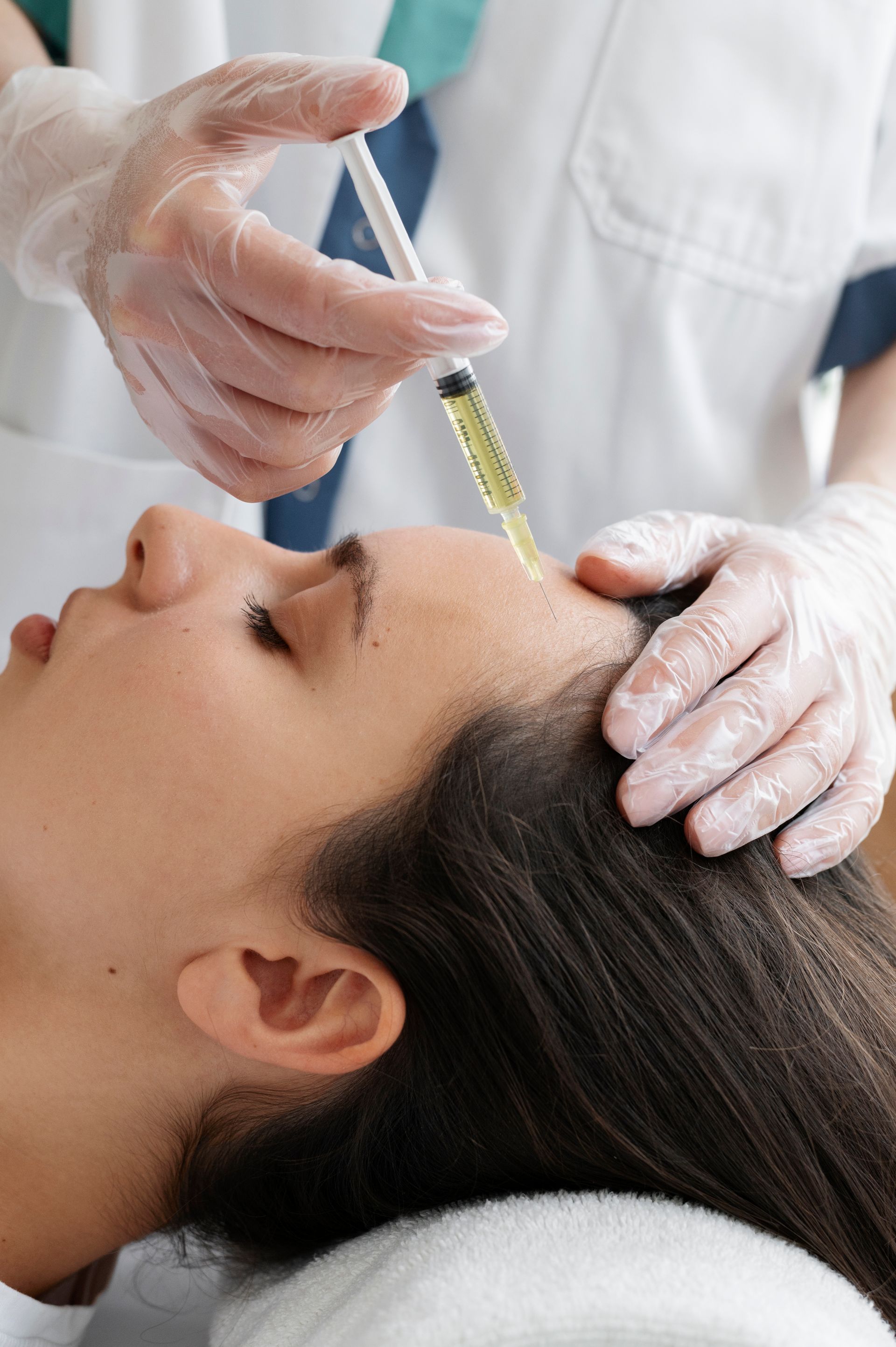 Cosmetic treatment with a syringe applied to a woman's forehead by gloved hands