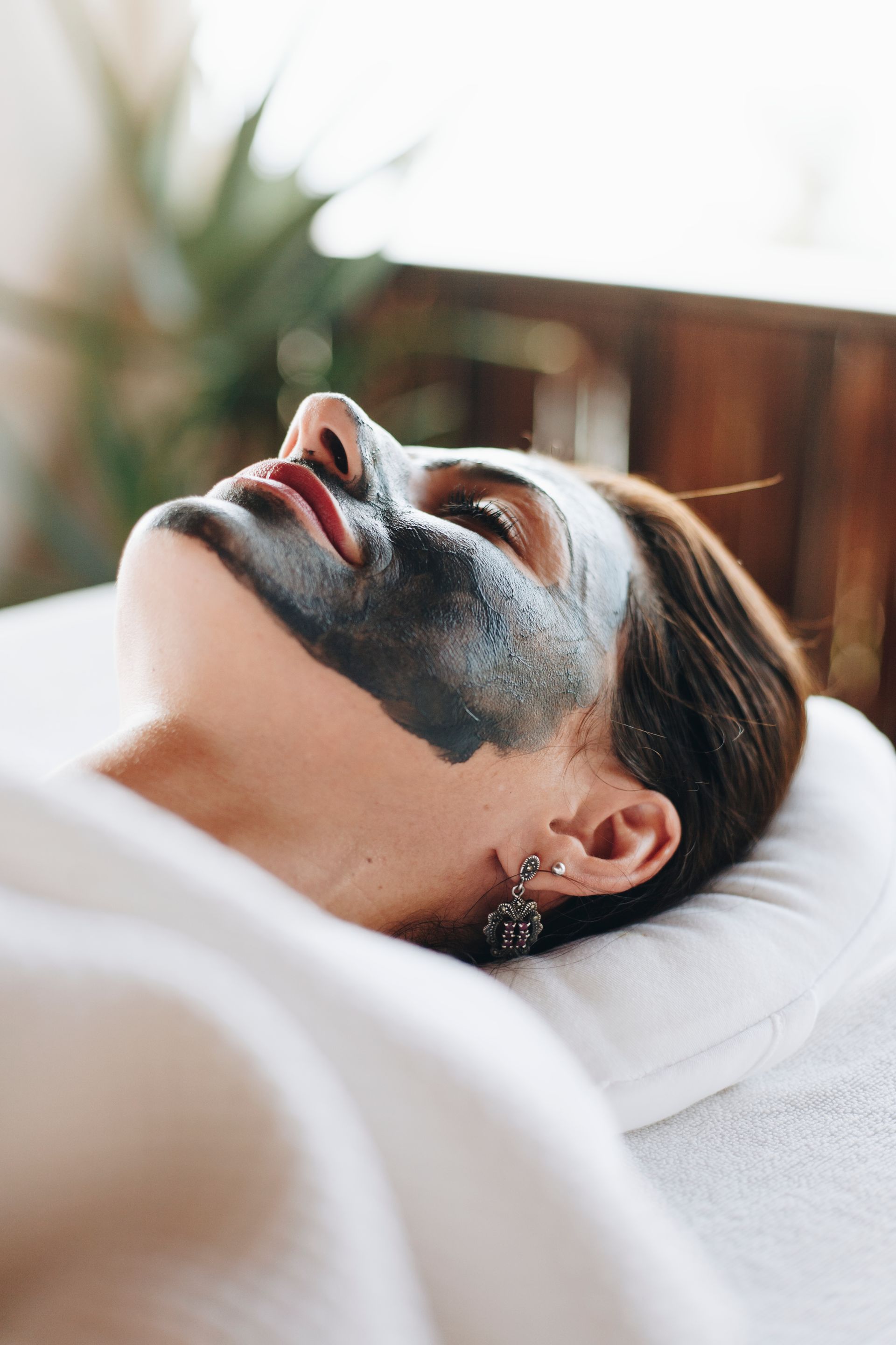 Person relaxing on a pillow with a black facial mask in a bright room