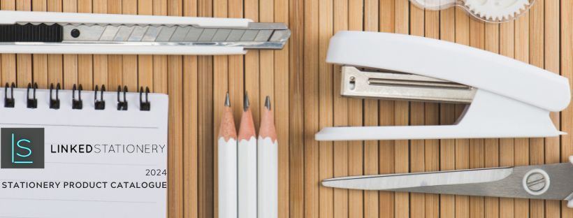 A stapler pencils scissors and a notebook are on a wooden table.