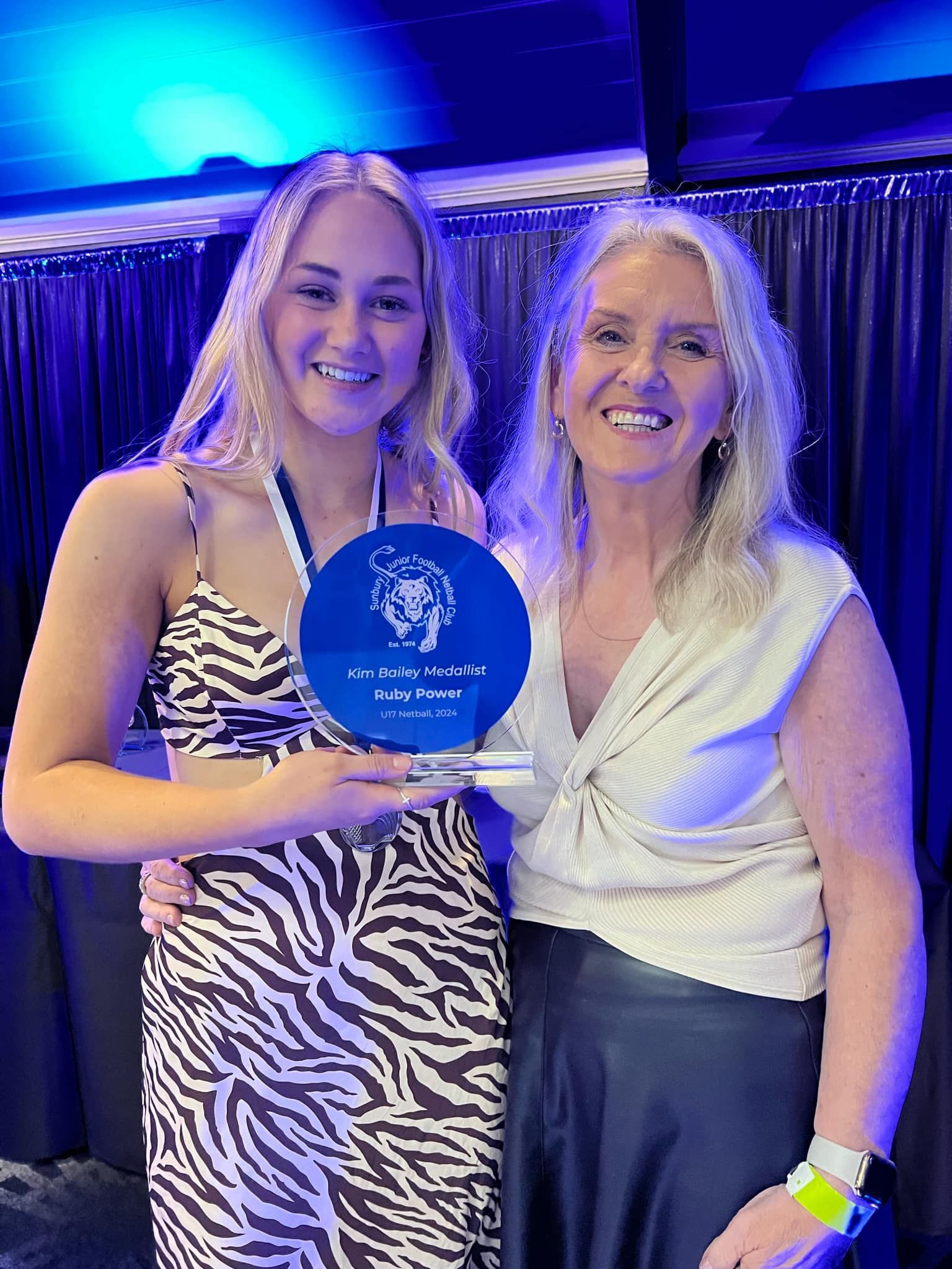 Two women are standing next to each other holding a trophy.