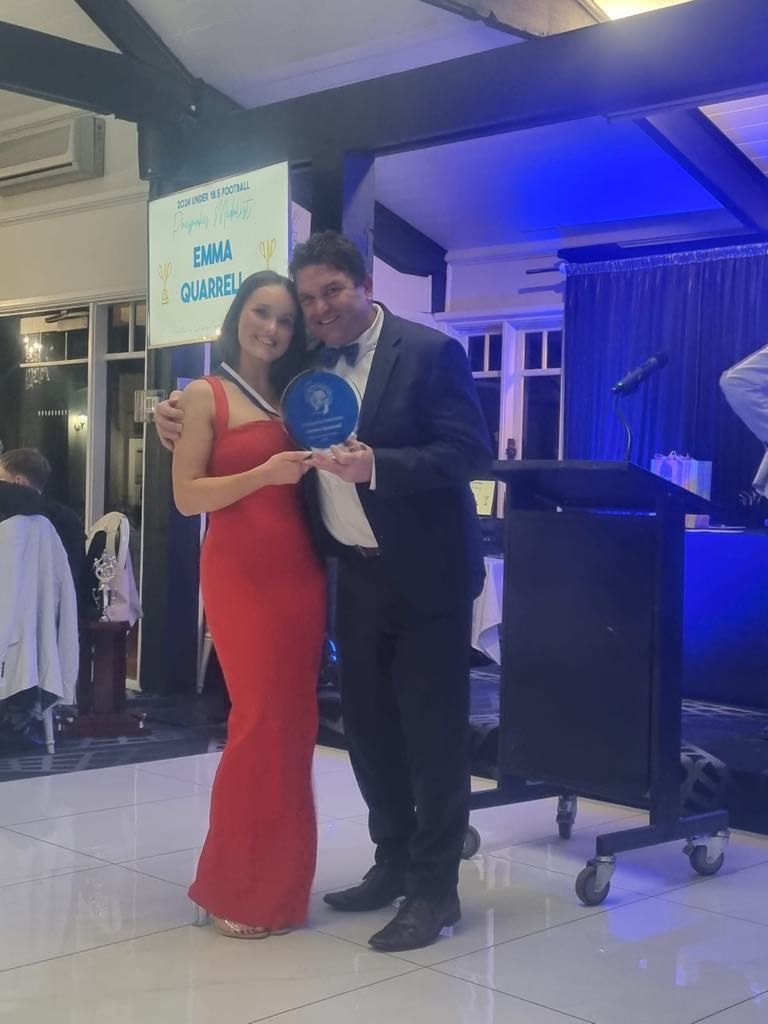 A man and a woman are standing next to each other in a room holding a trophy.