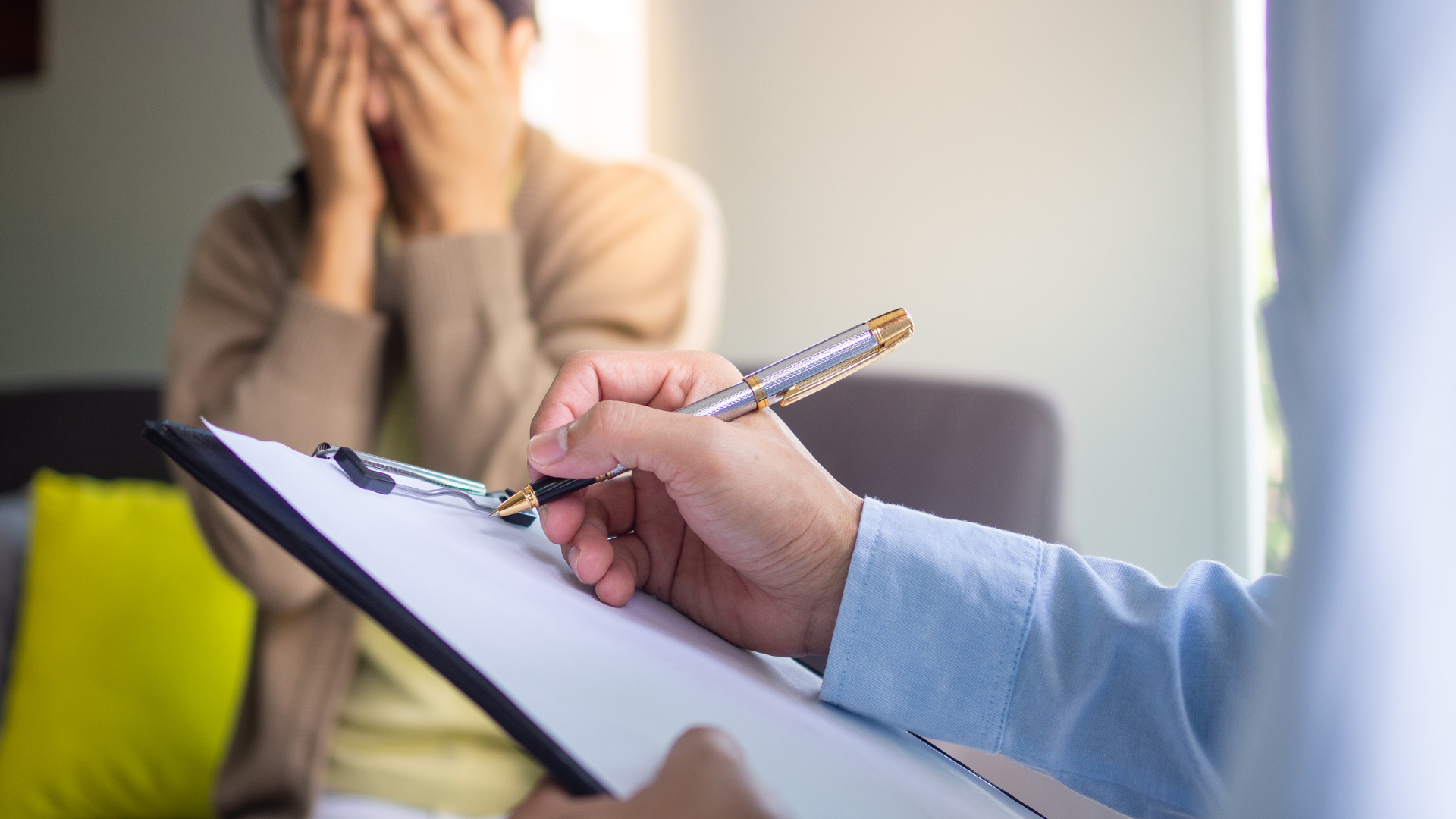 Therapist taking notes as a person cries, covering their face in a home office setting.