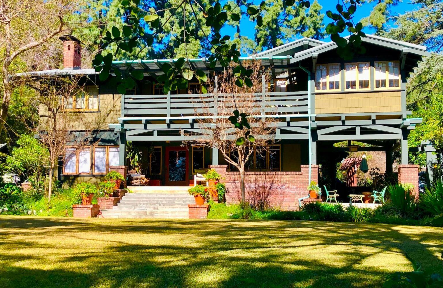 Craftsman-style house with green facade, red brick accents, and a large front lawn under a bright sky.