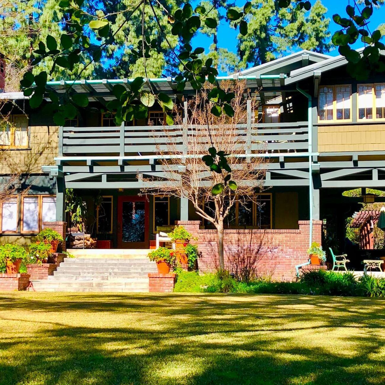 Two-story Craftsman home with a large porch and a green lawn under a bright blue sky.