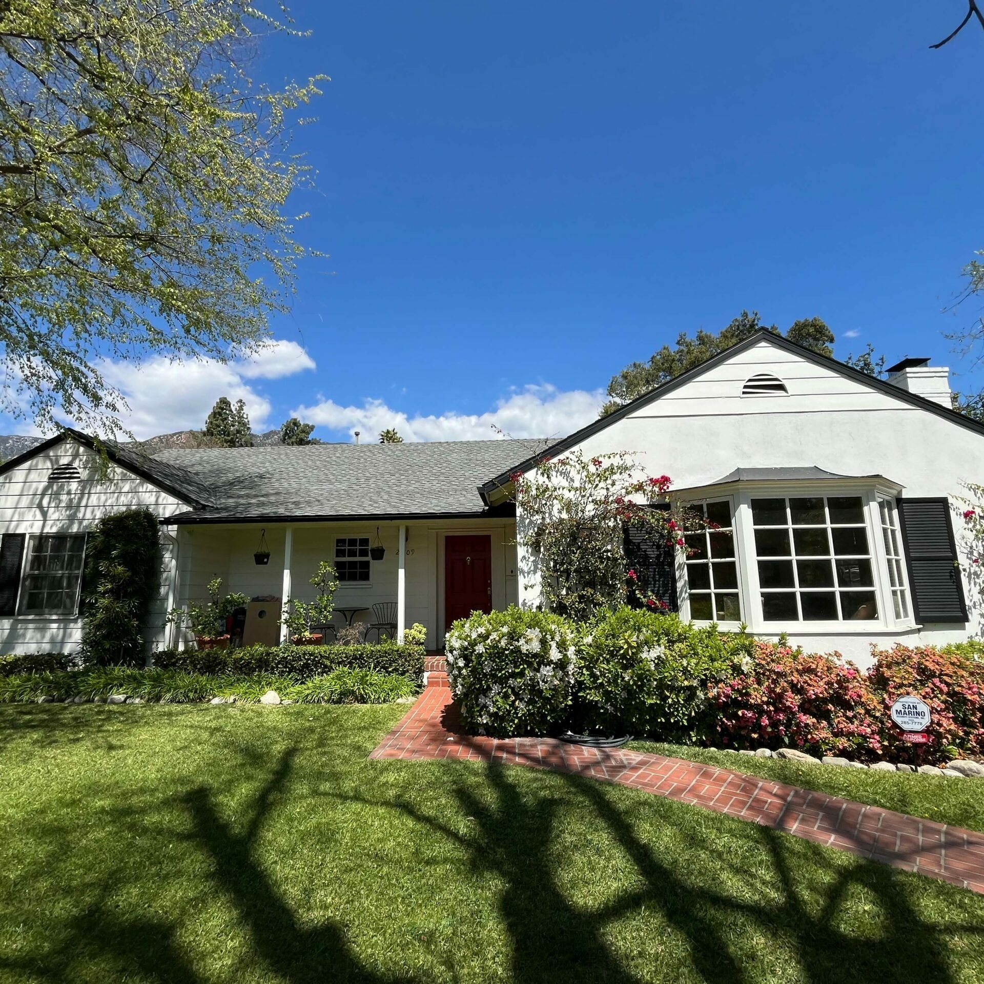 White house with red door, brick walkway, and green lawn under a blue sky.