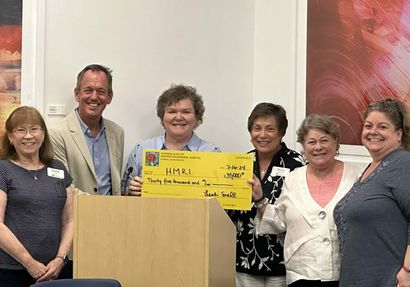 Group of people holding a large check at a podium. They appear to be celebrating a donation.