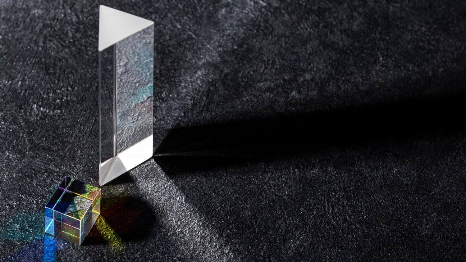 Ein Prisma bricht das Licht und erzeugt so ein Regenbogenspektrum auf einer dunklen, strukturierten Oberfläche.