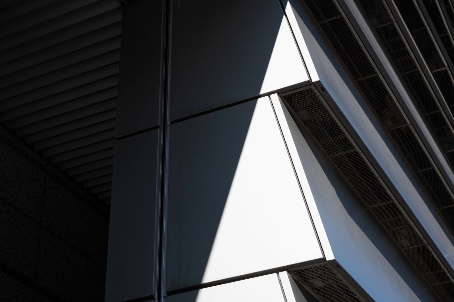 Nahaufnahme einer modernen Gebäudeecke mit geometrischen Paneelen und kontrastreichen Schatten.