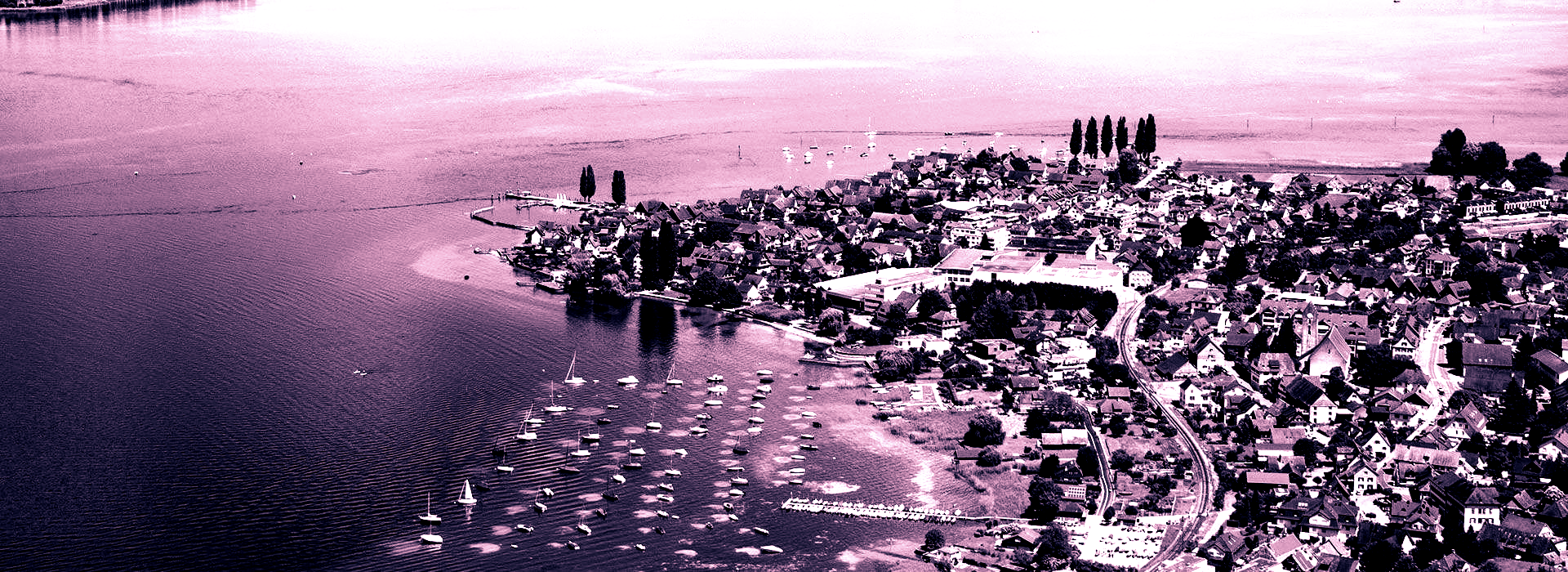 Luftaufnahme einer Uferlinie mit einem Gewässer im Vordergrund und Personen, die am Ufer stehen.