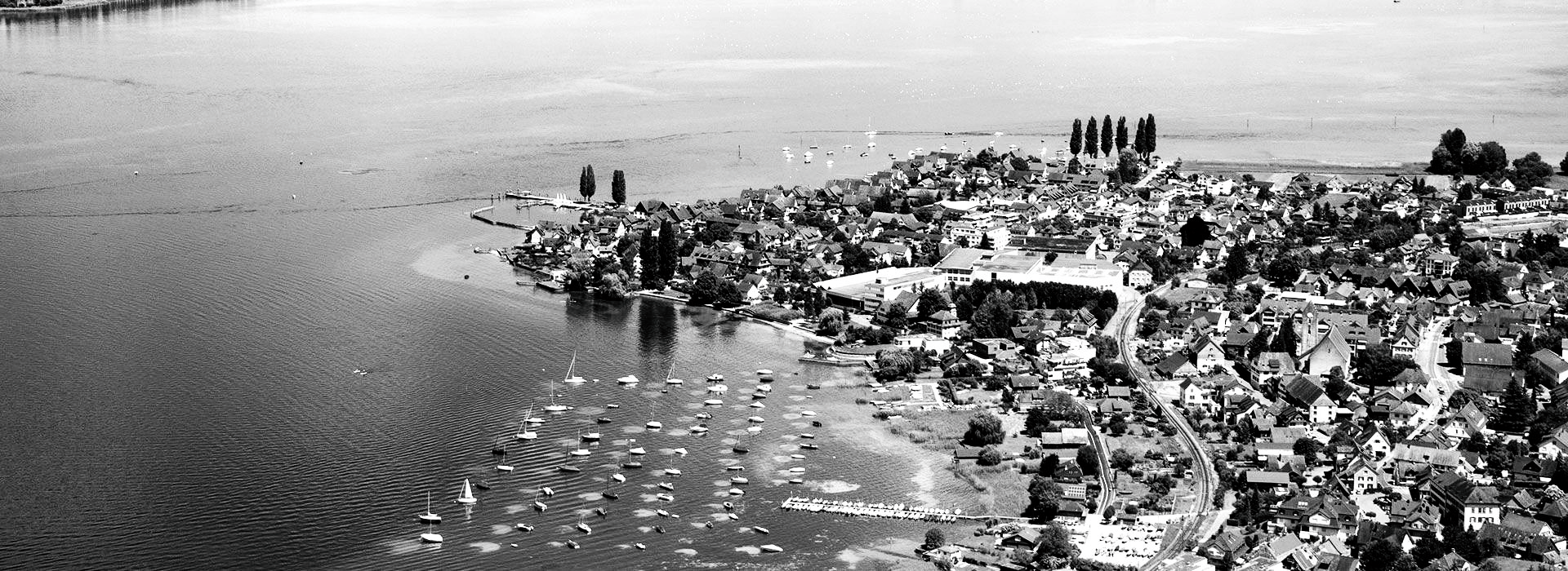 Luftaufnahme einer Uferlinie mit einem Gewässer im Vordergrund und Personen, die am Ufer stehen.