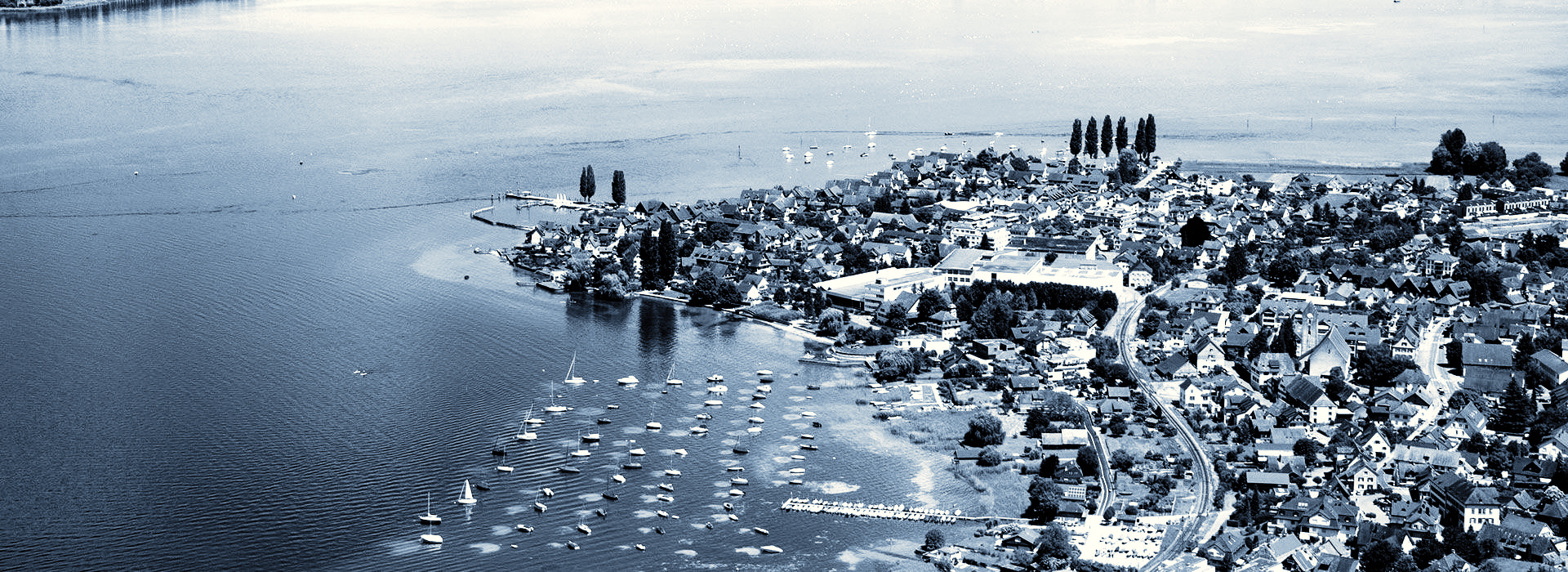 Luftaufnahme einer Uferlinie mit einem Gewässer im Vordergrund und Personen, die am Ufer stehen.