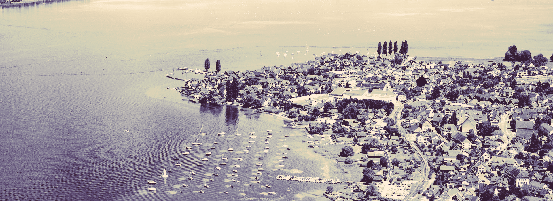 Luftaufnahme einer Uferlinie mit einem Gewässer im Vordergrund und Personen, die am Ufer stehen.