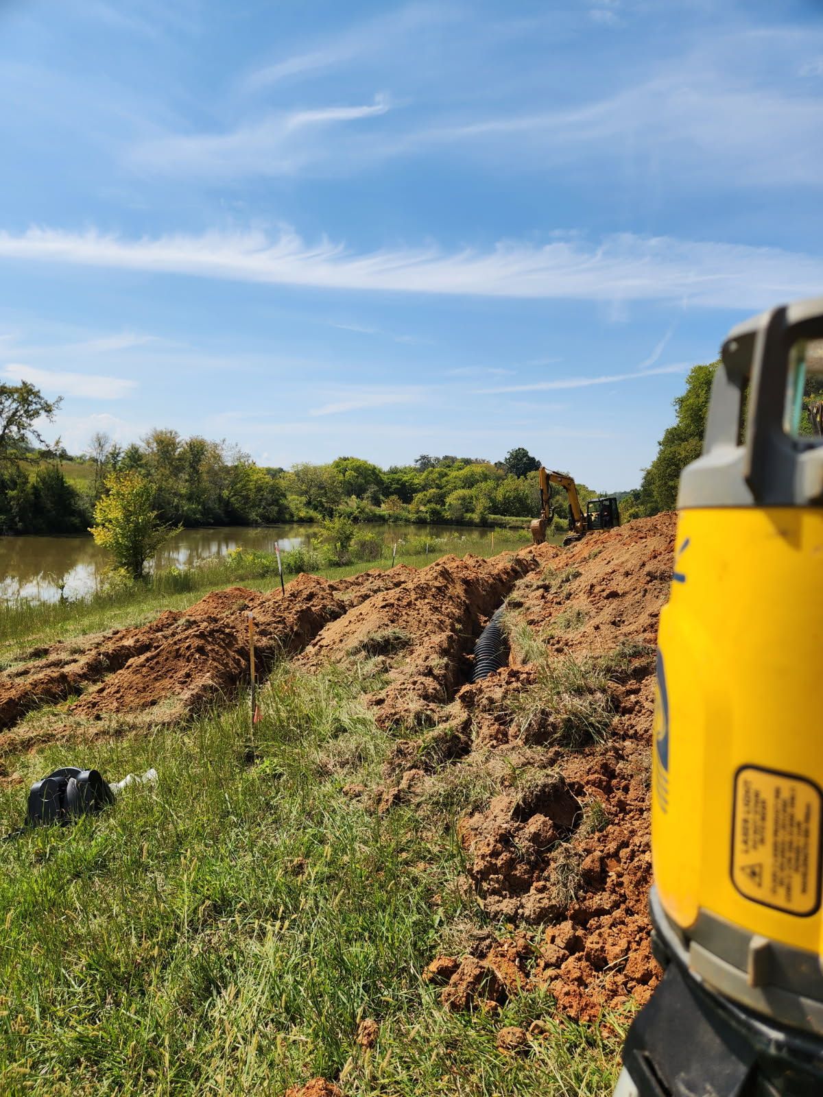 A trench filled with black drainage pipes surrounded by red dirt, in an outdoor setting.