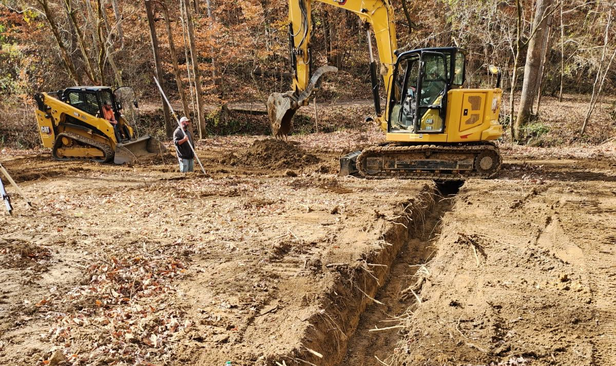 Aerial view: Three yellow construction vehicles on a muddy construction site, likely earthmoving.
