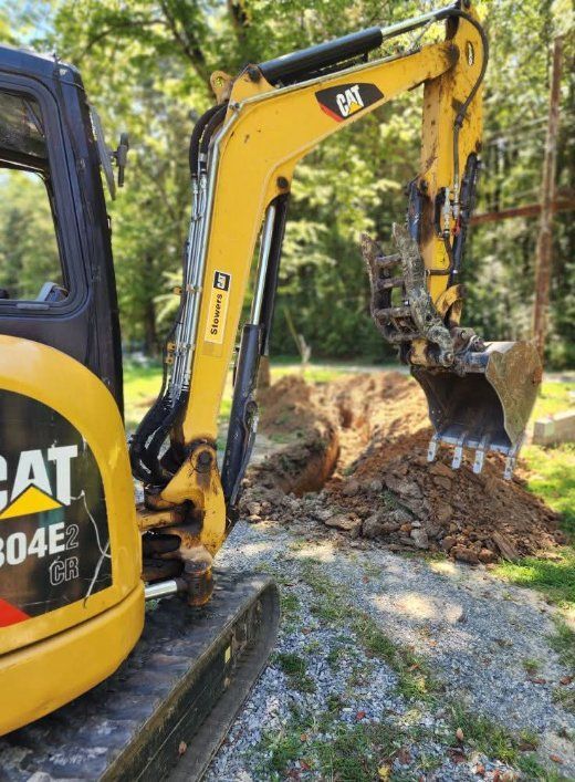 Overhead view of an excavator digging at a construction site, with piles of dirt next to it.