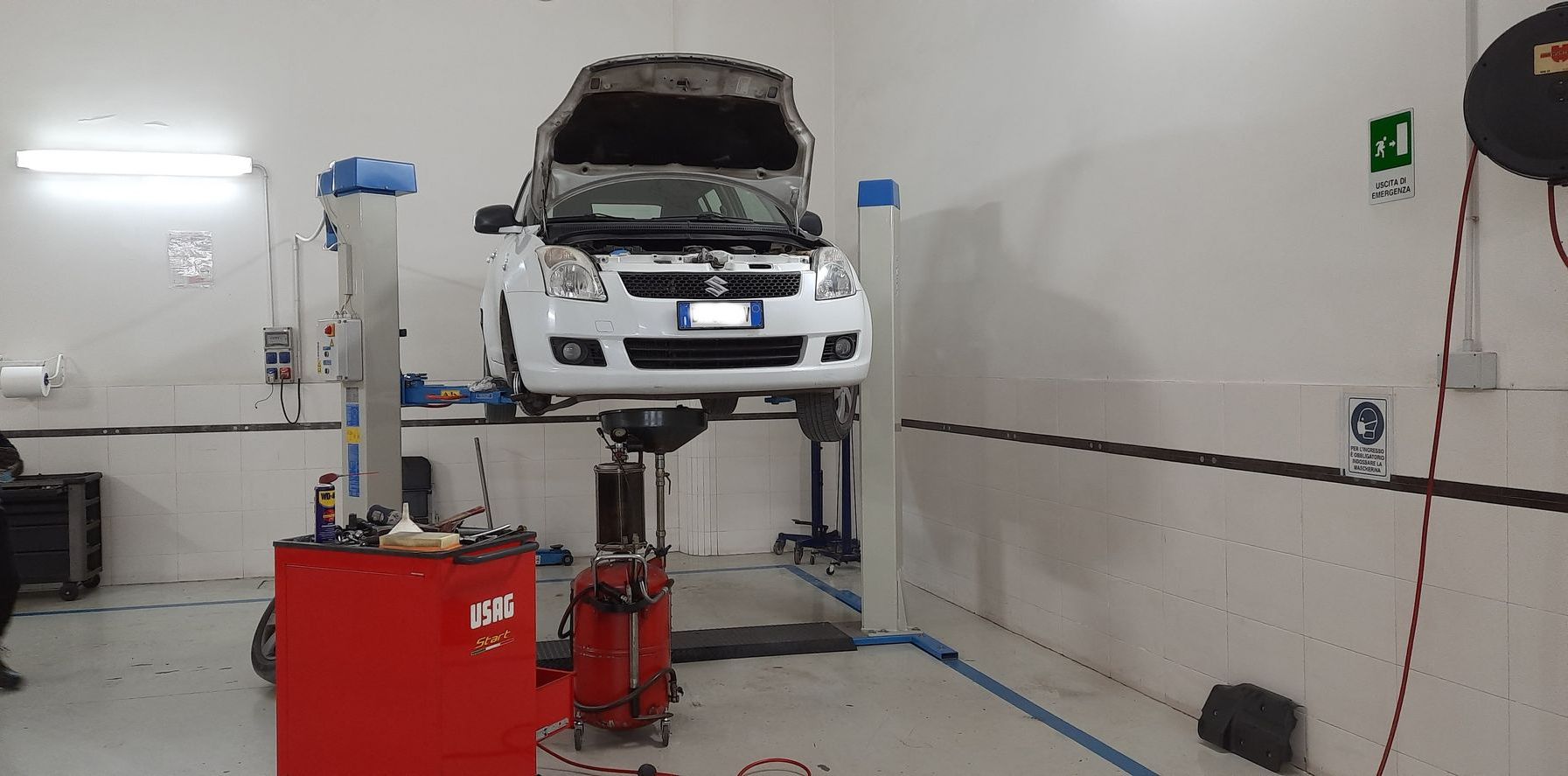 Un'auto bianca è parcheggiata su un ponte elevatore in un garage.