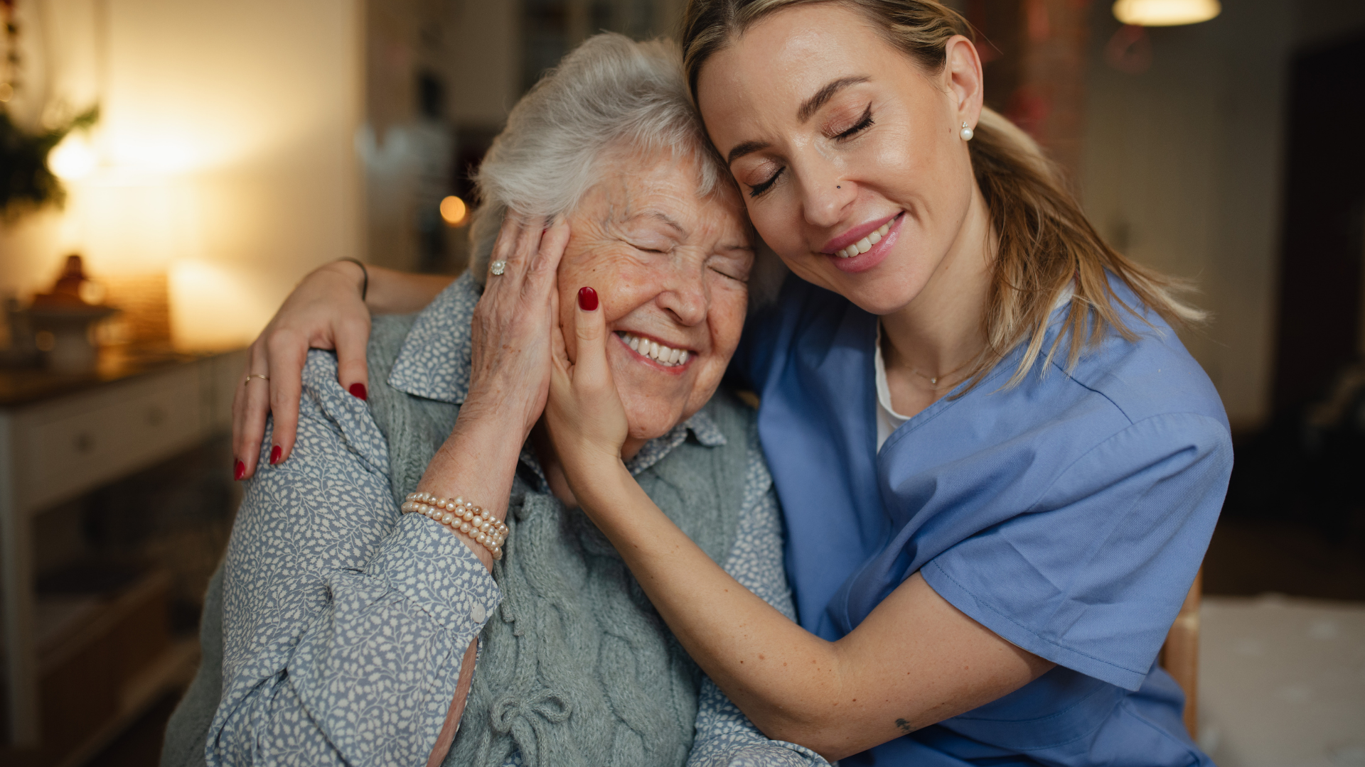 Nurse in red scrubs giving water to a sick elderly woman in bed.