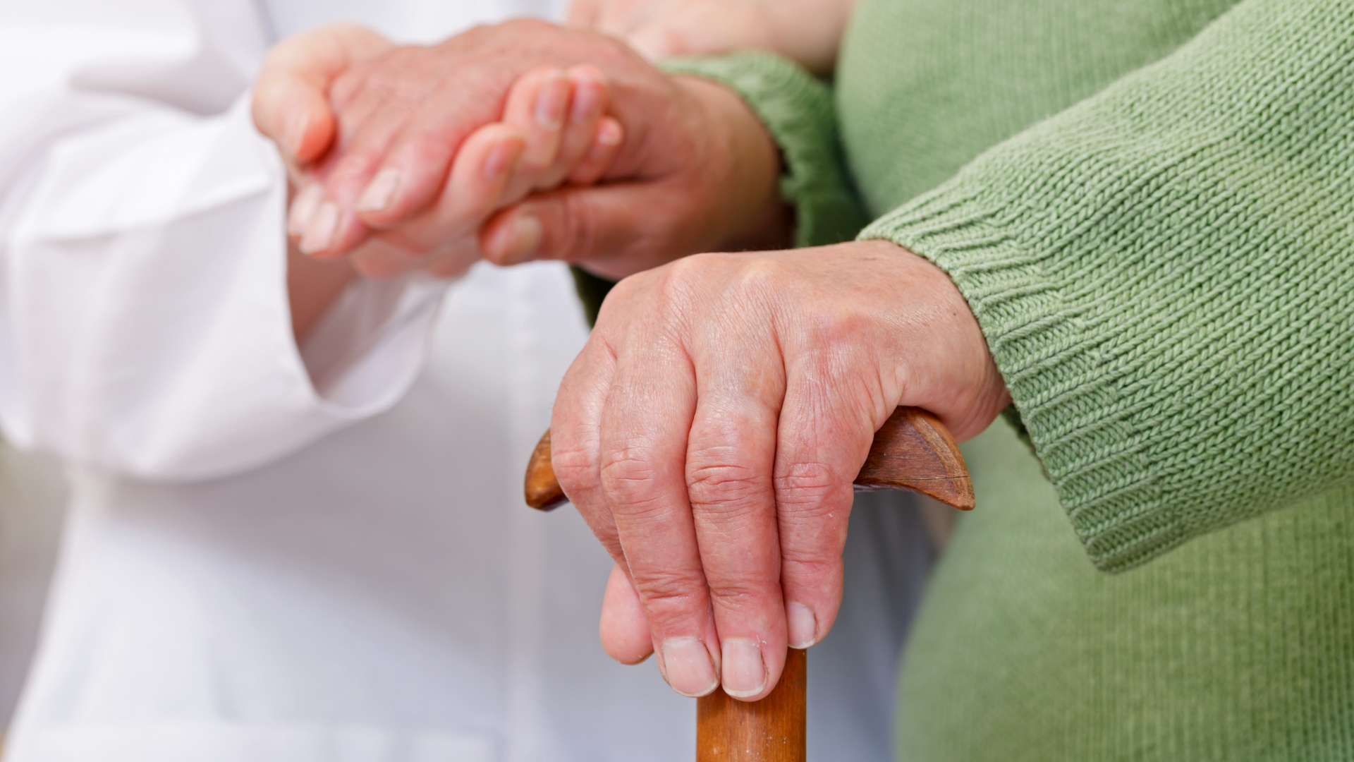 A healthcare worker checks an elderly woman's blood pressure in a living room.