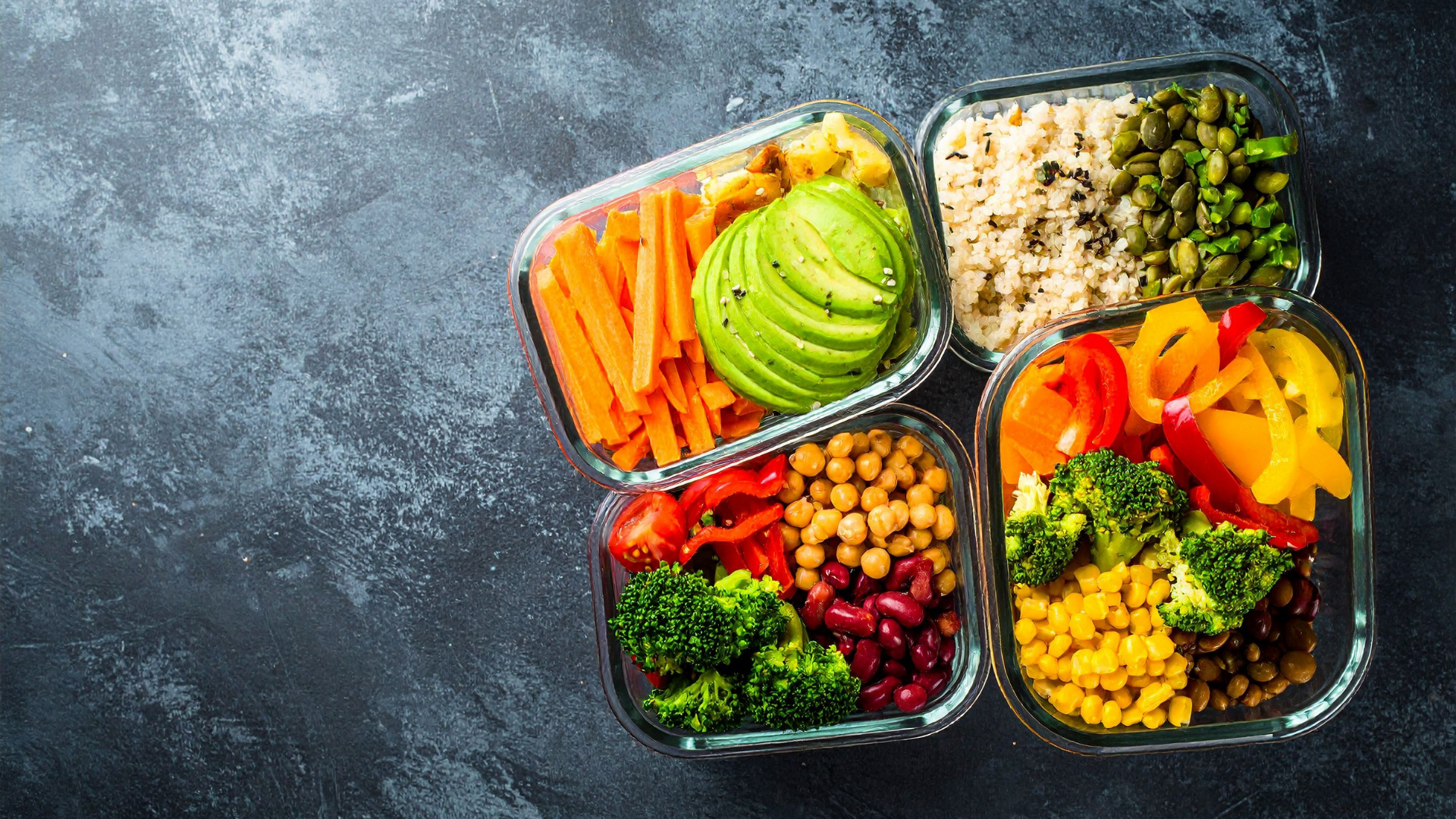 Overhead view of four glass containers filled with colorful, plant-based meal prep components: carrots, avocado, broccoli, chickpeas, beans, rice, and peppers.