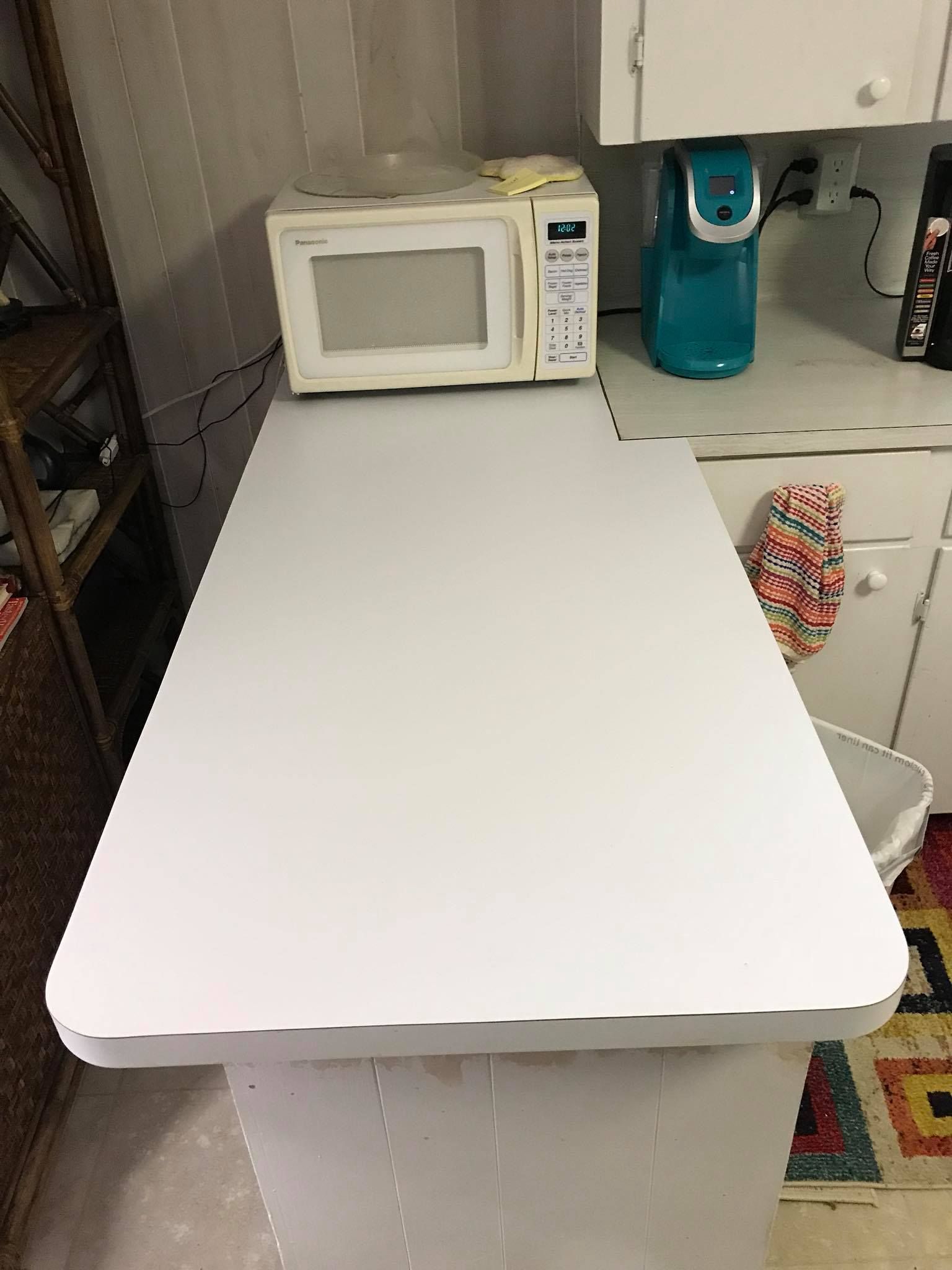 A white kitchen counter with a microwave and a teal coffee maker on top, set against white cabinets.