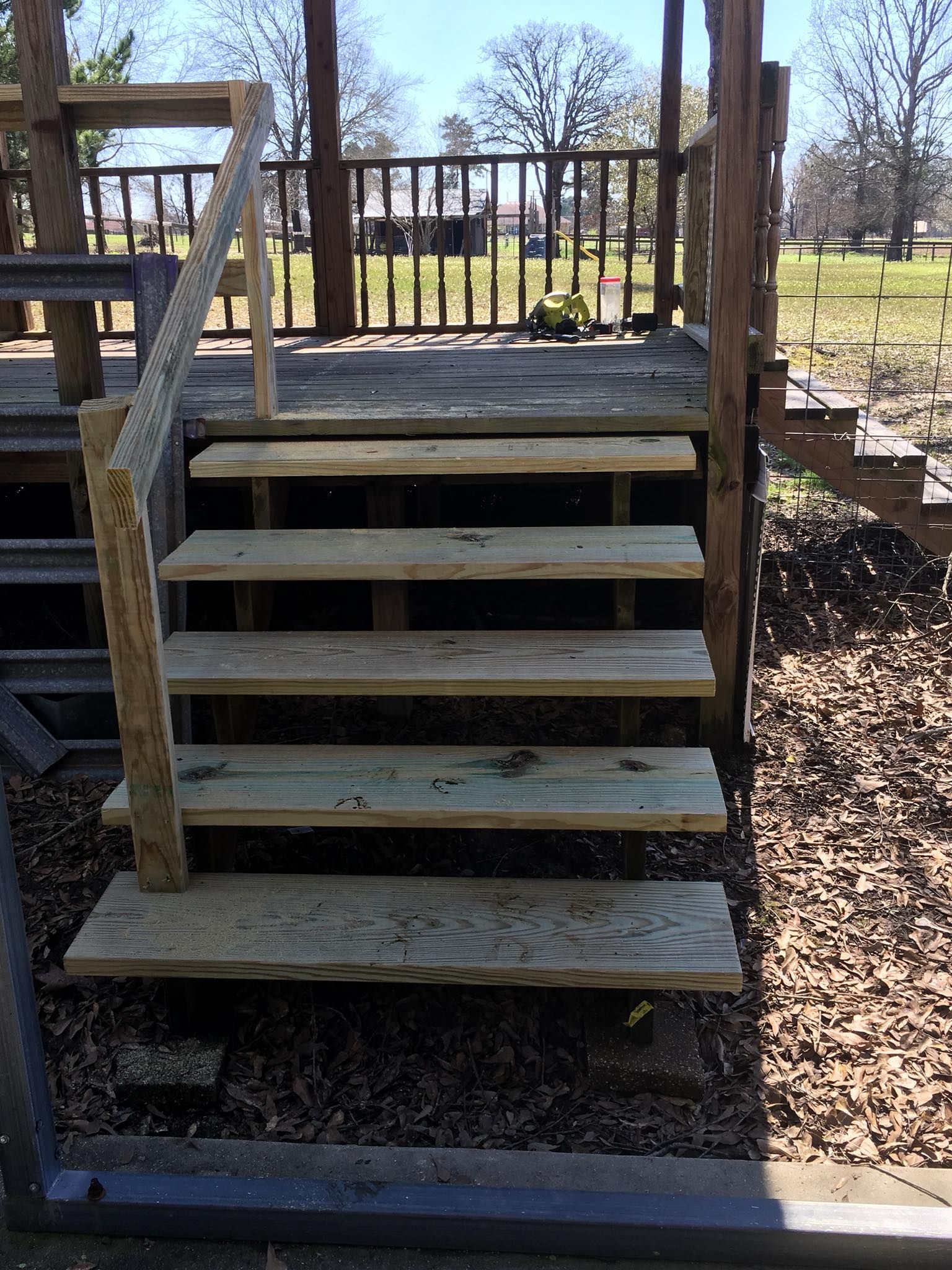 Wooden stairs with a single handrail leading up to a raised deck platform outdoors.