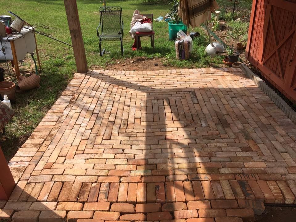 A herringbone-pattern brick patio under a wooden structure in a backyard.