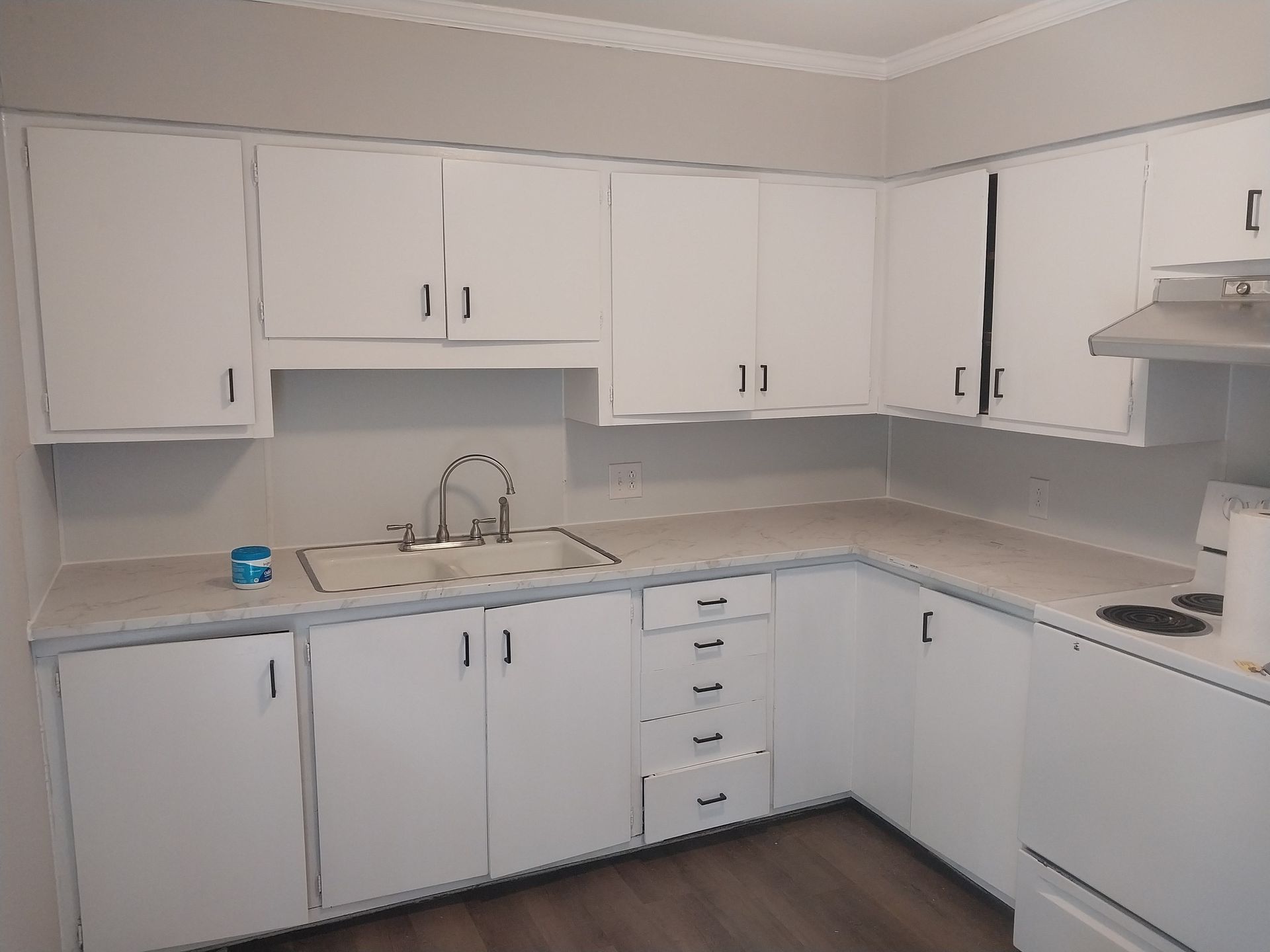 White kitchen cabinets, countertop, sink, and stovetop in a corner layout.