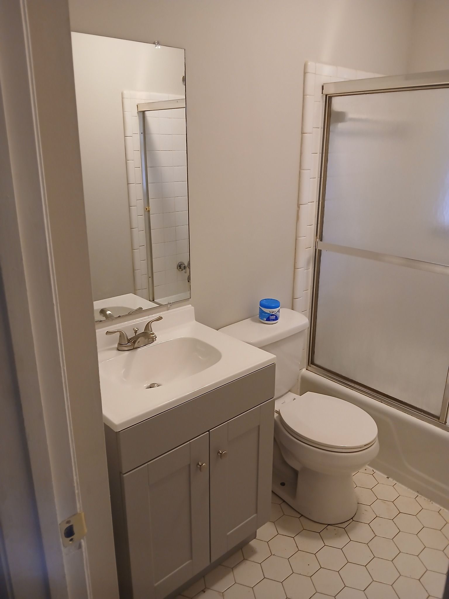 Bathroom with gray vanity, white toilet, and shower with frosted glass. White and gray tiled floor.