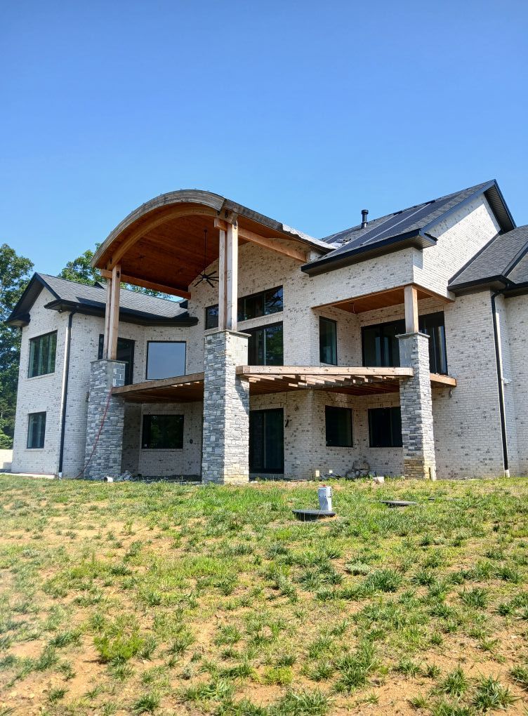 Two-story brick house with a wooden deck and arched roof, set against a blue sky.