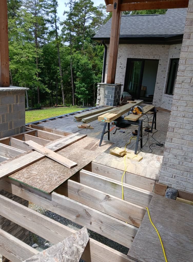 Deck construction in progress; wooden beams, plywood, and tools on patio.