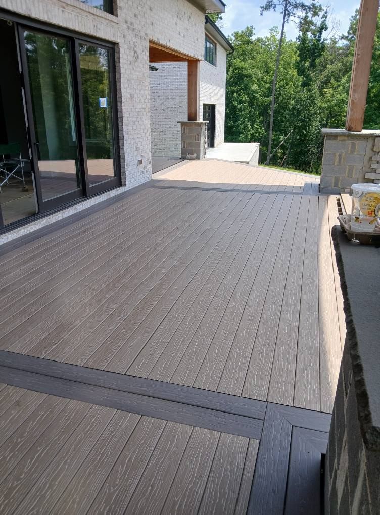 Composite deck with dark border, adjacent to a brick house and lush greenery.