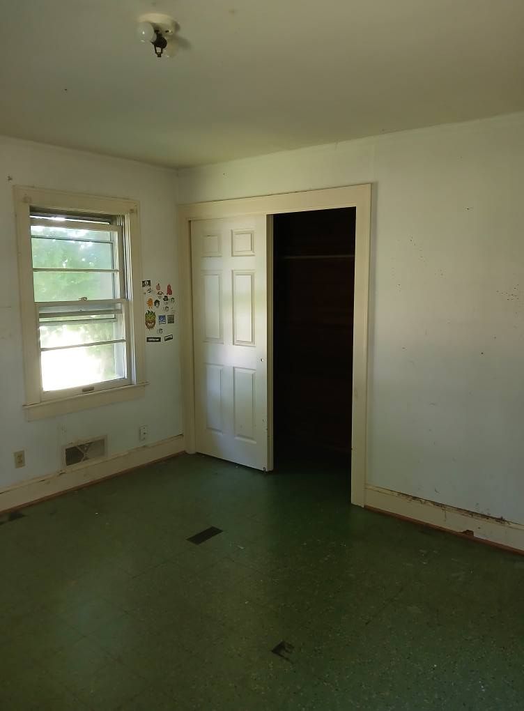 Empty room with green floor, white walls, closet with closed doors, and a window.