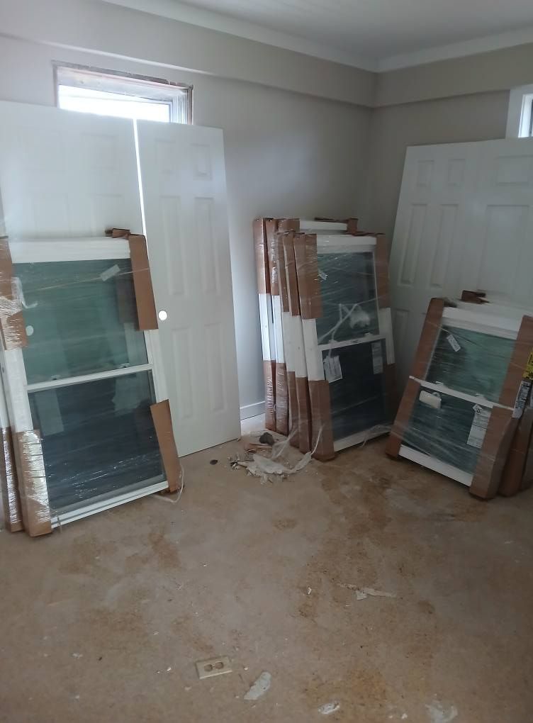 Room with new windows and doors, still wrapped in protective materials, on a light-colored floor.