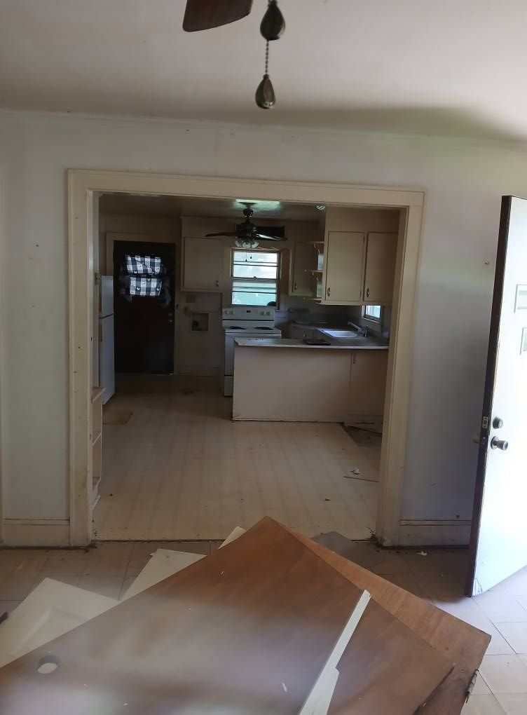 Interior view of a house. Open doorway leads to a kitchen with cabinets, and a doorway to a room with a refrigerator.