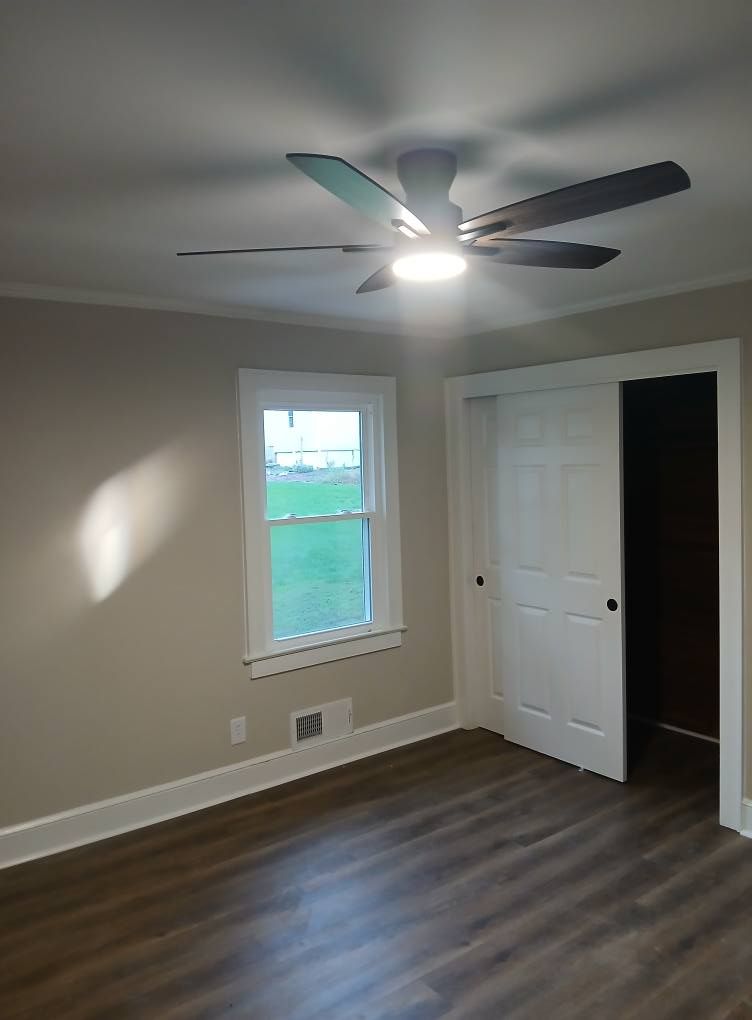 Bedroom with ceiling fan, window, white sliding door, and wood-look flooring. Walls are beige.