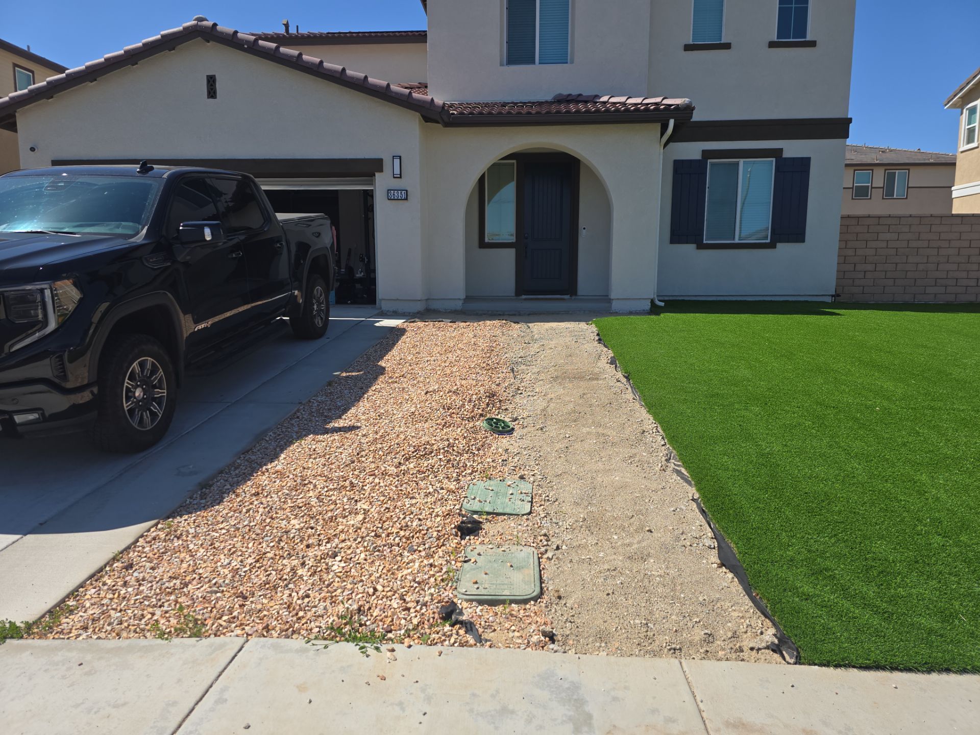 House with a truck in the driveway. A walkway is covered in gravel, with a patch of green grass to the right.