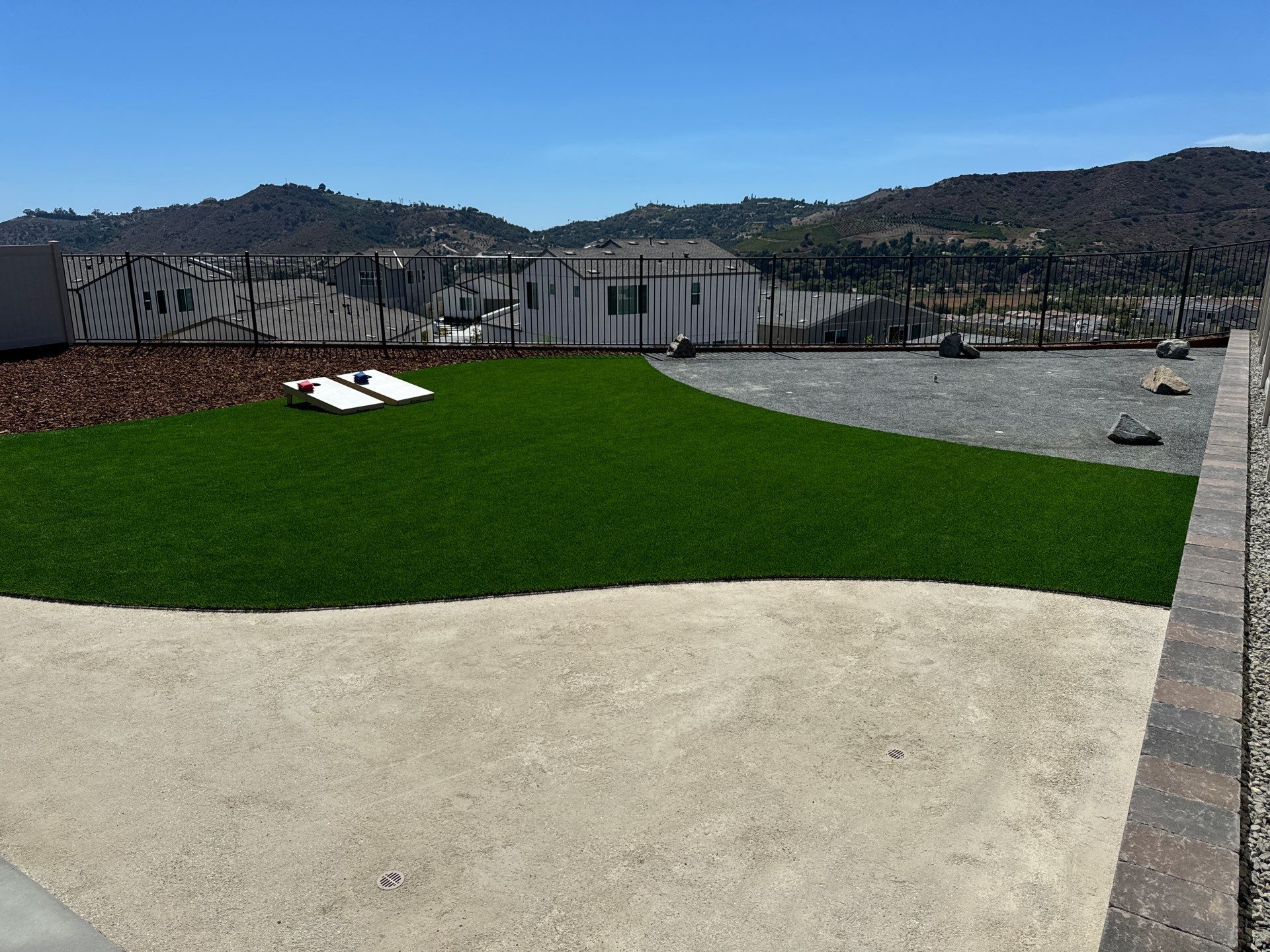 Green artificial turf, gravel, and rock landscaping against a backdrop of hills and a clear blue sky.