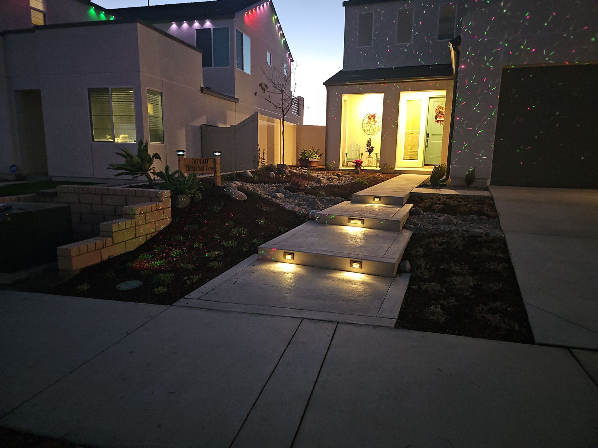 Night view of a house with illuminated front steps and landscaping. Christmas lights and star projector are visible.