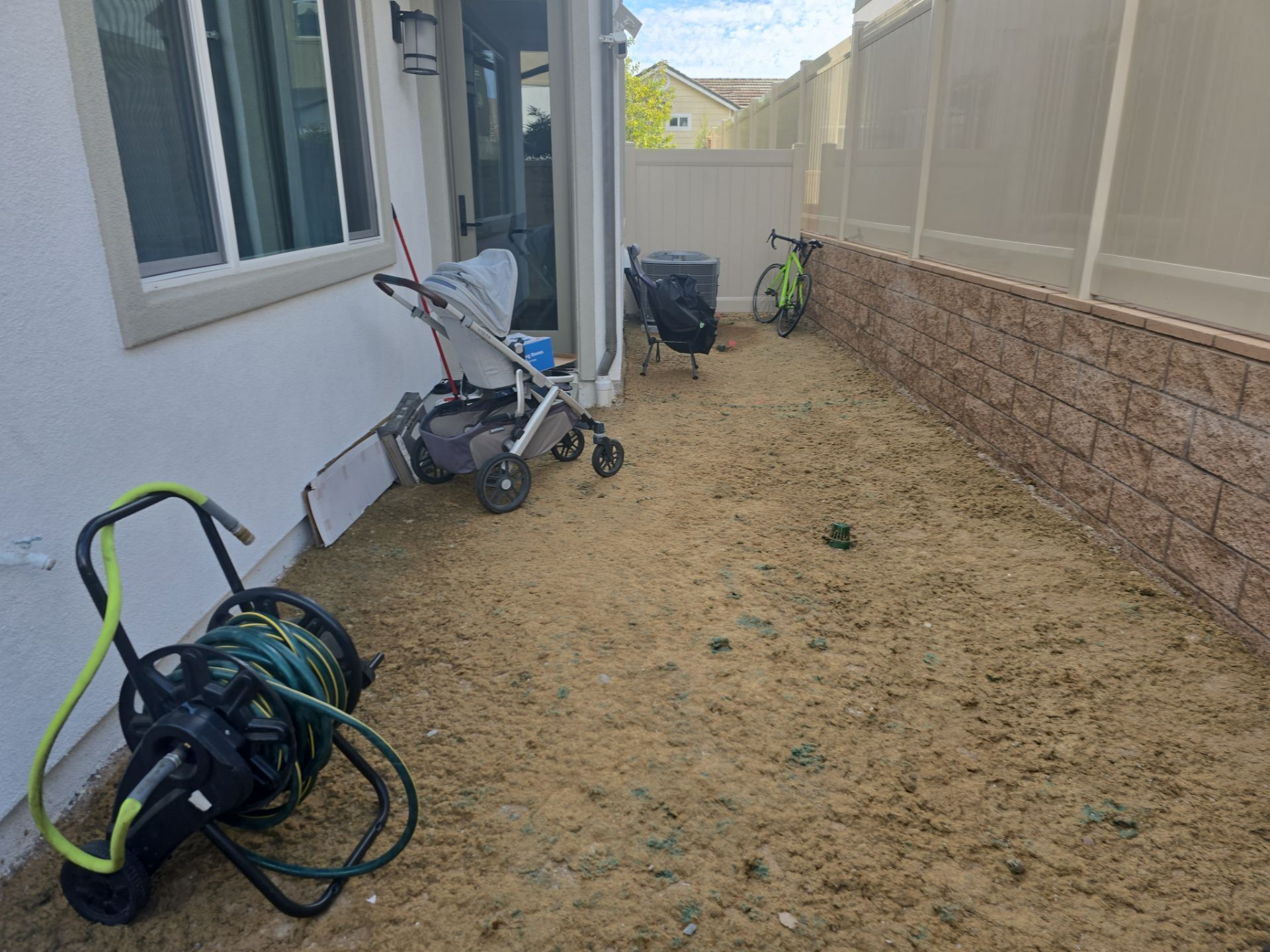 Backyard with tan mulch, a stroller, hose, and a bicycle.