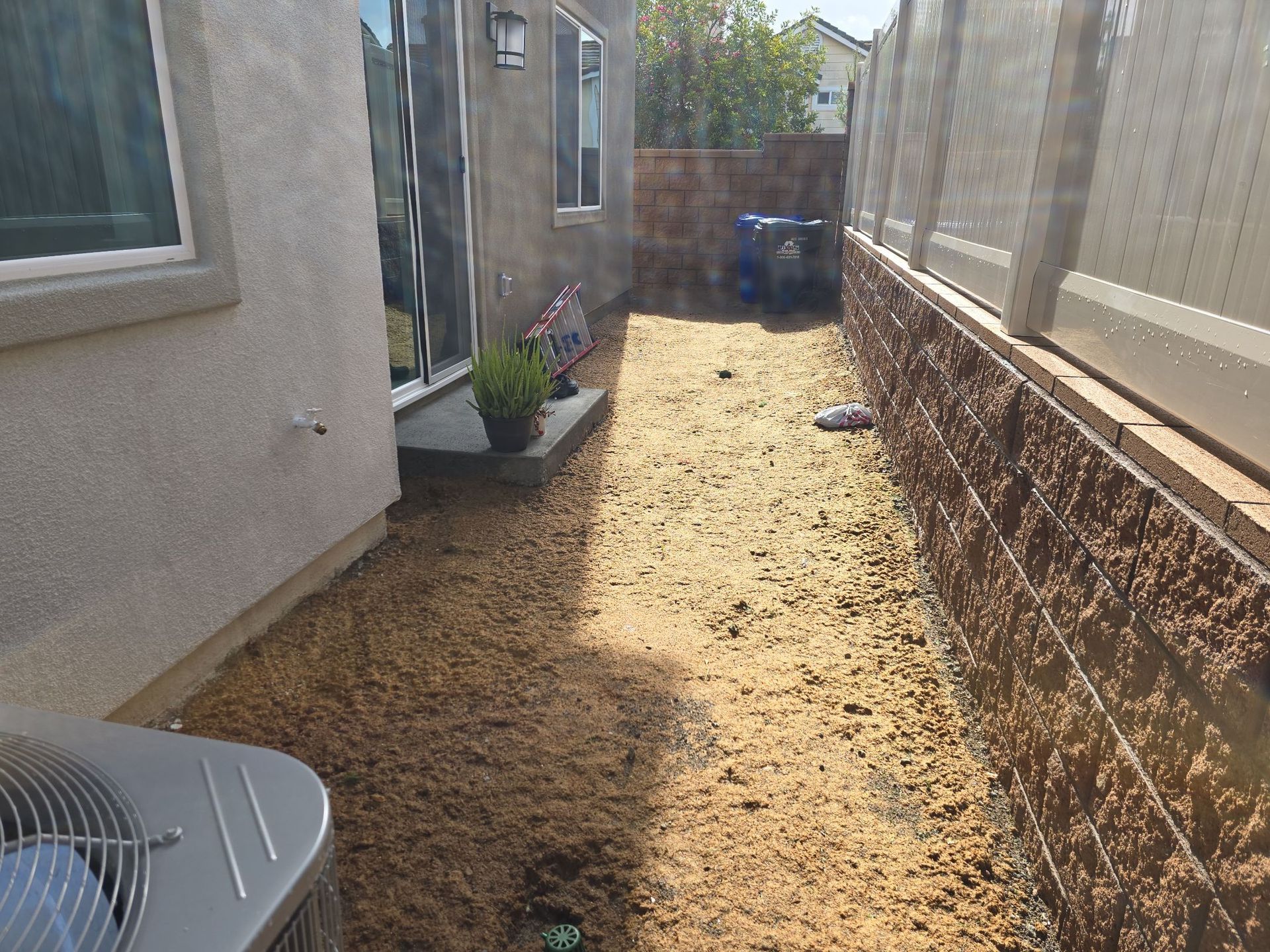 Narrow backyard with dirt and mulch between a house and a brick wall.