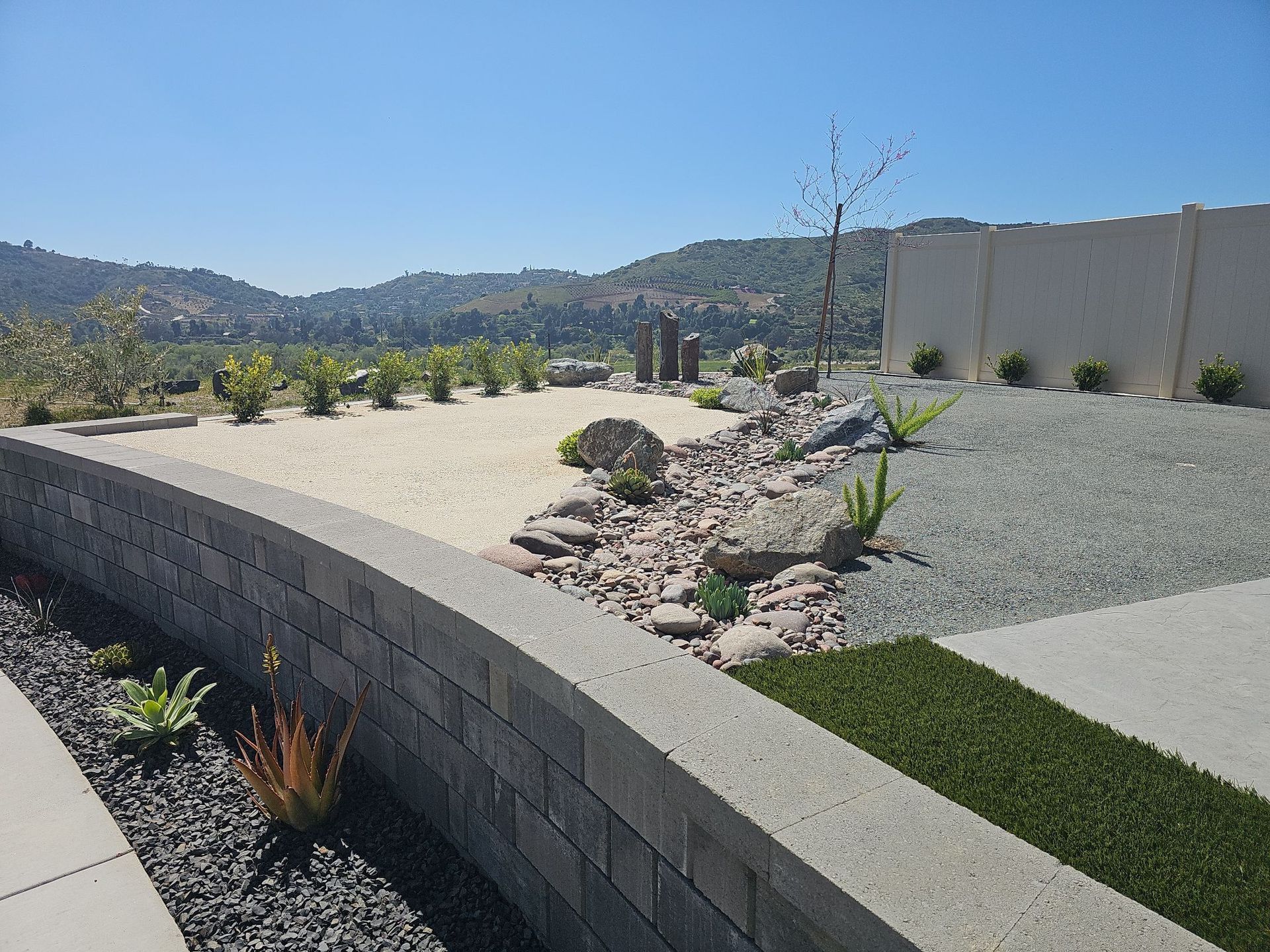 Landscaped yard with retaining wall, gravel, and drought-tolerant plants, overlooking a distant valley under a sunny sky.