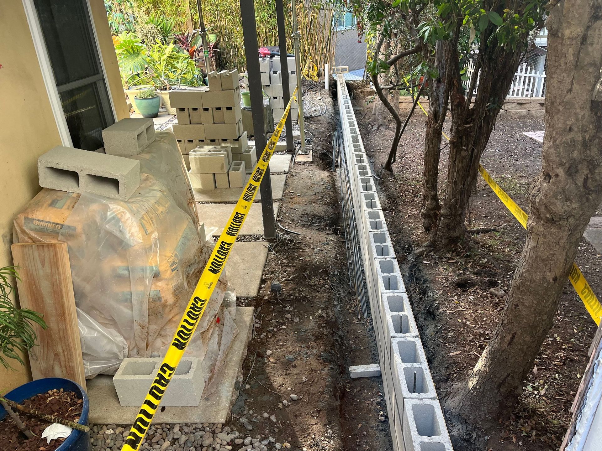 Construction of a cinder block wall, outdoors, with caution tape and building materials.