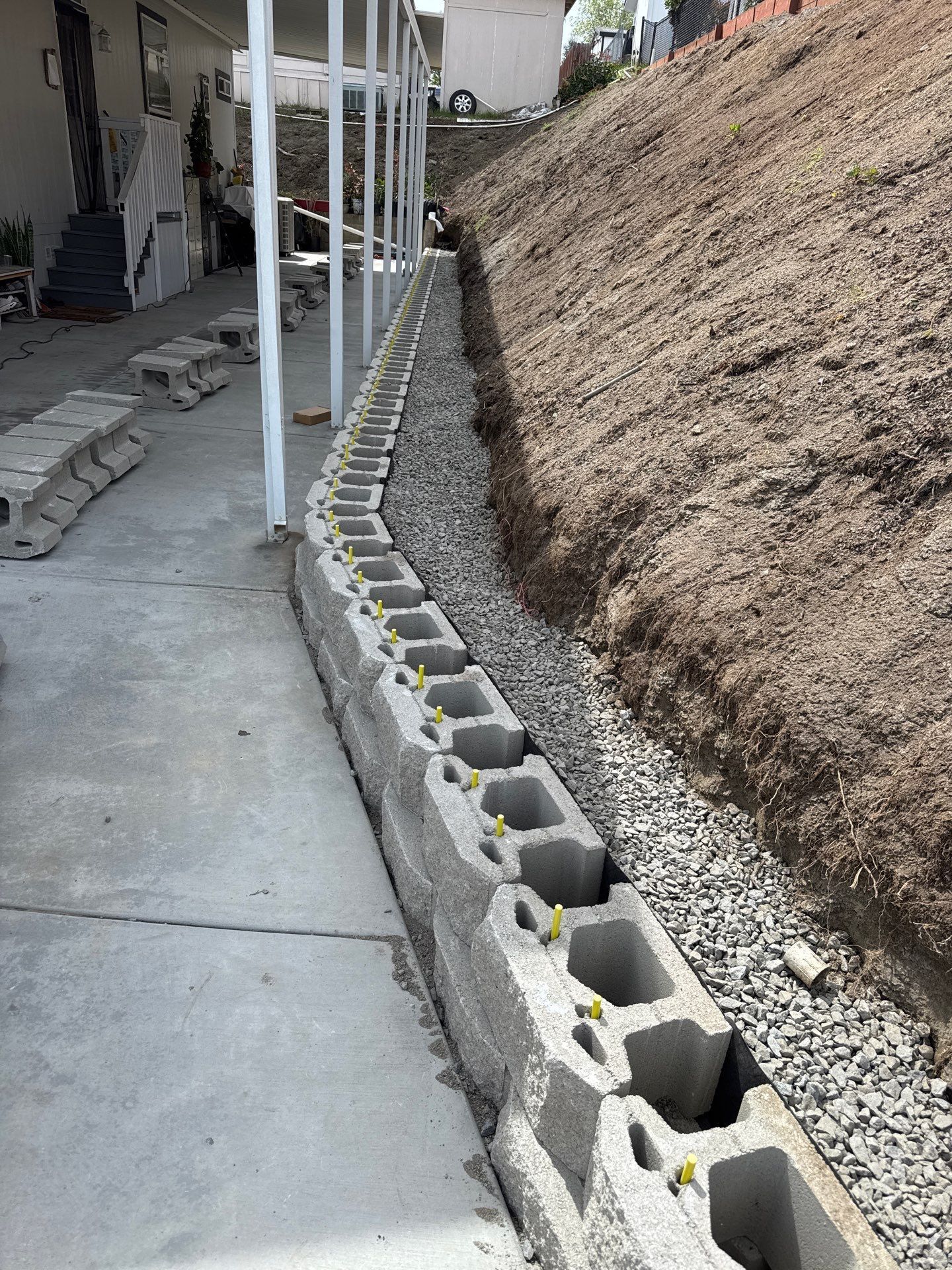 Concrete block retaining wall next to a concrete walkway, supporting a sloped hillside.