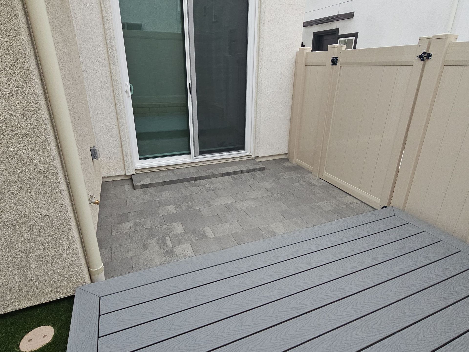 Patio with gray pavers, composite deck, sliding glass door, and beige fence.