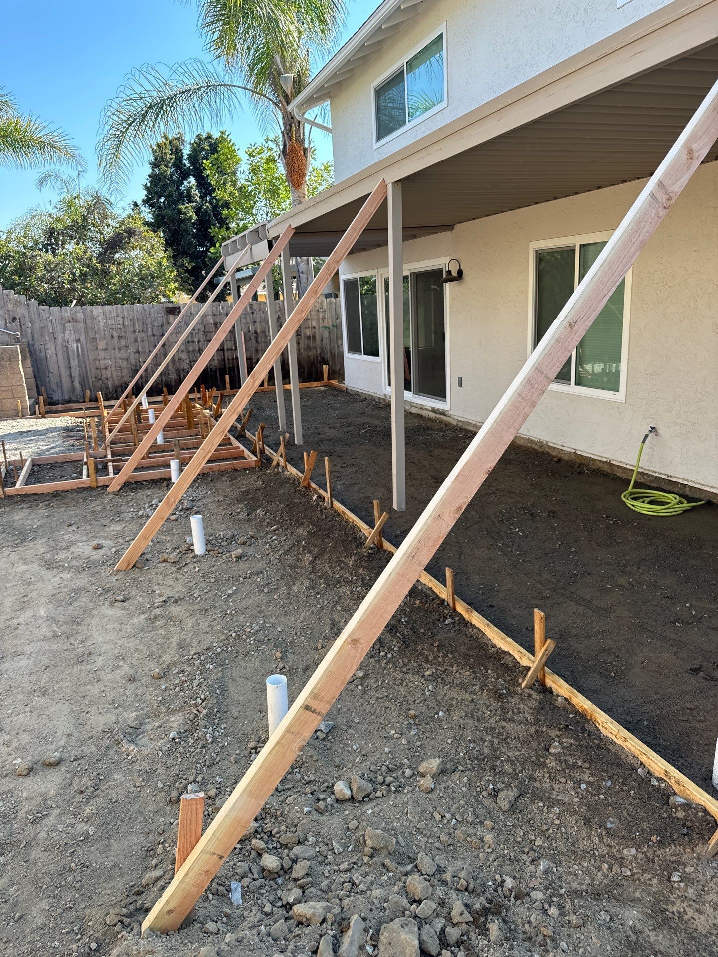 Construction site: wooden supports next to a house, prepared for pouring concrete in a backyard.