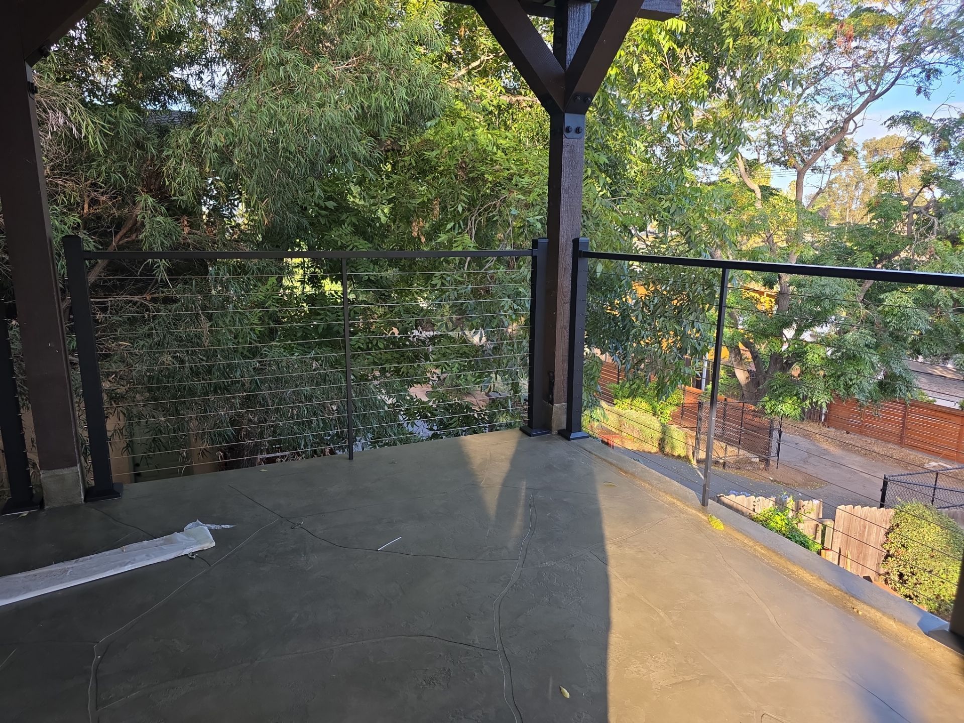 Patio with black railing, glass panels, and trees in the background, shadowed area on the floor.