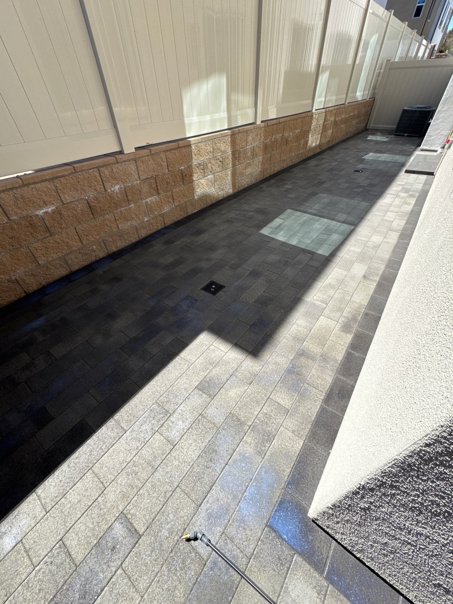 Long, narrow outdoor pathway paved with dark gray blocks, with brick wall and concrete wall on sides.