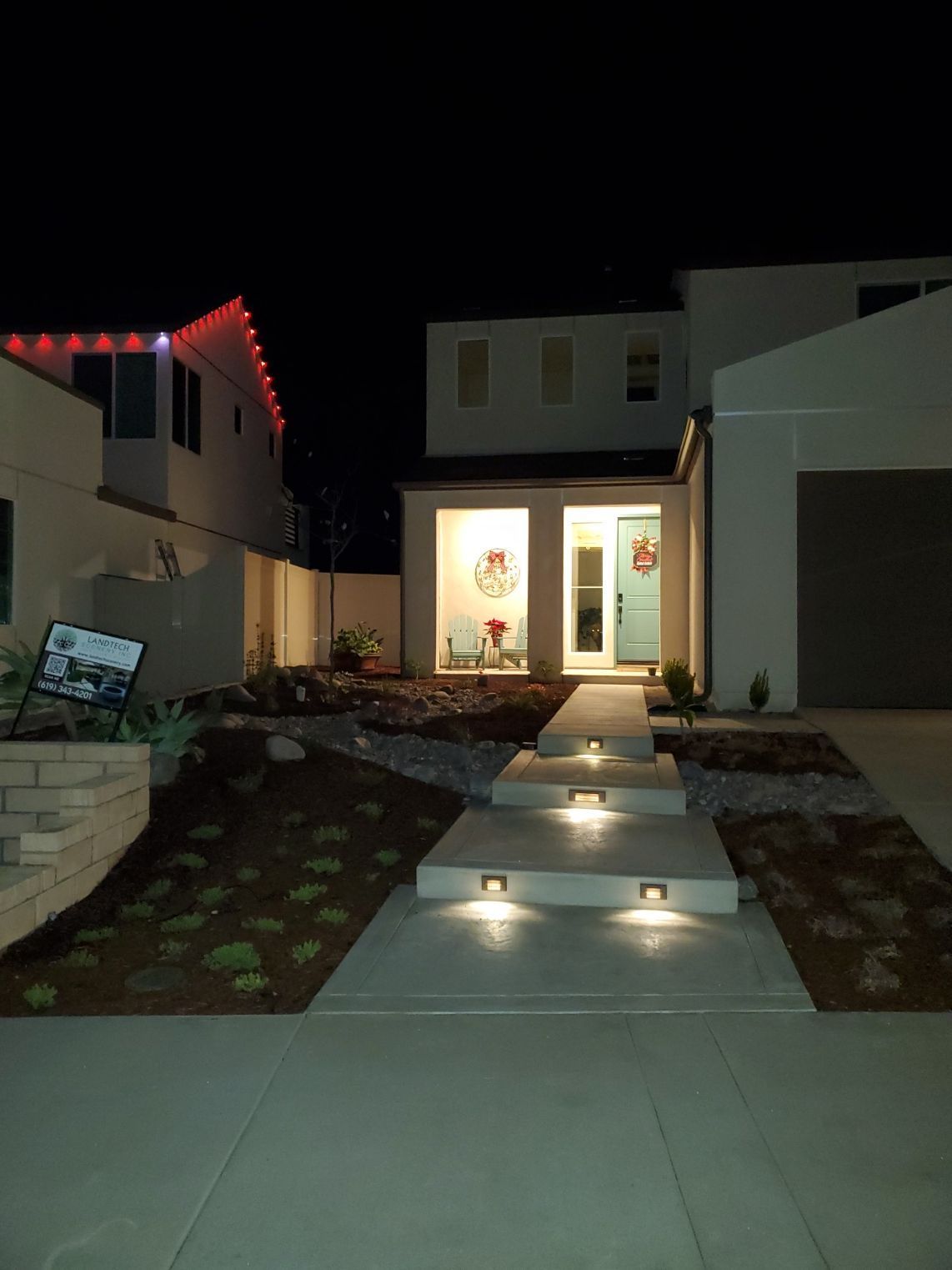 Night view of a modern home with lighted steps leading to a front door. Christmas lights decorate the roof.