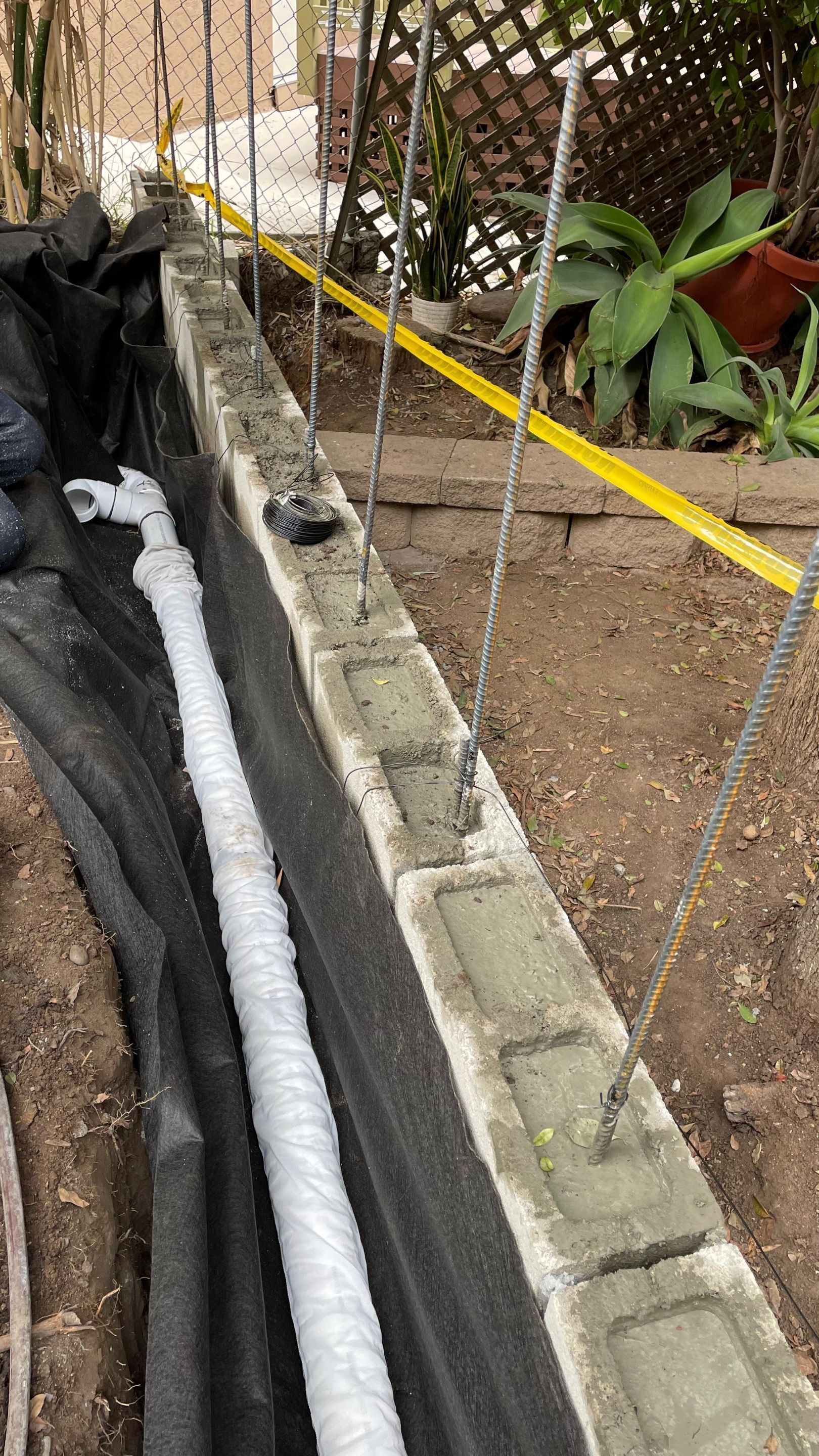 Concrete block retaining wall under construction with rebar and a wrapped pipe.