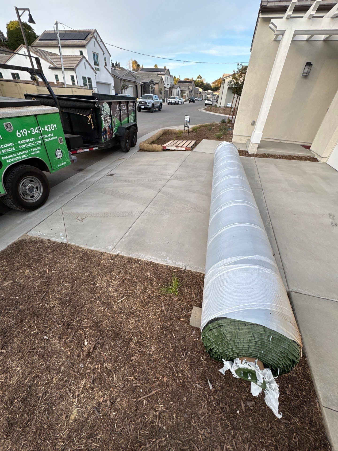 Roll of green artificial turf on driveway next to a landscaping truck.